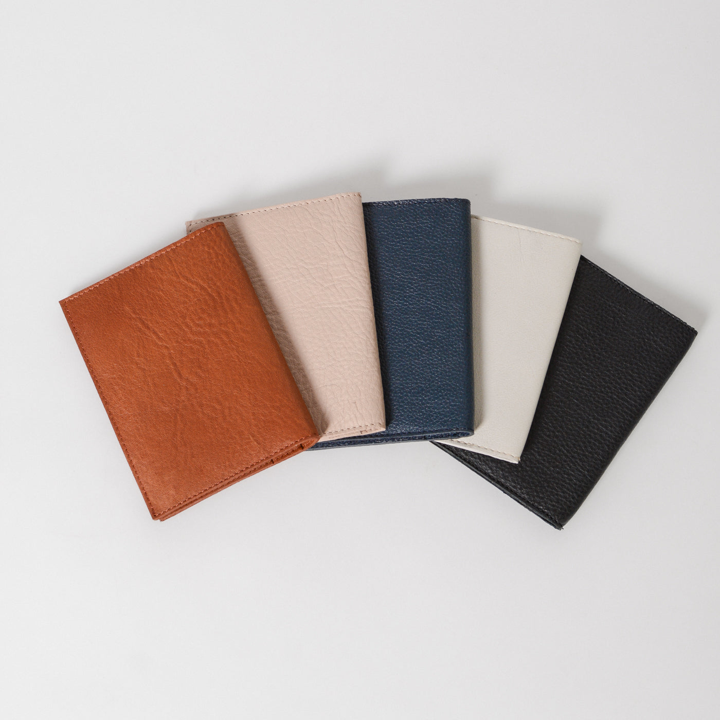 A collection of slim full-grain leather travel wallets in various colors including brown, beige, blue, and black, displayed in a fan-like arrangement.