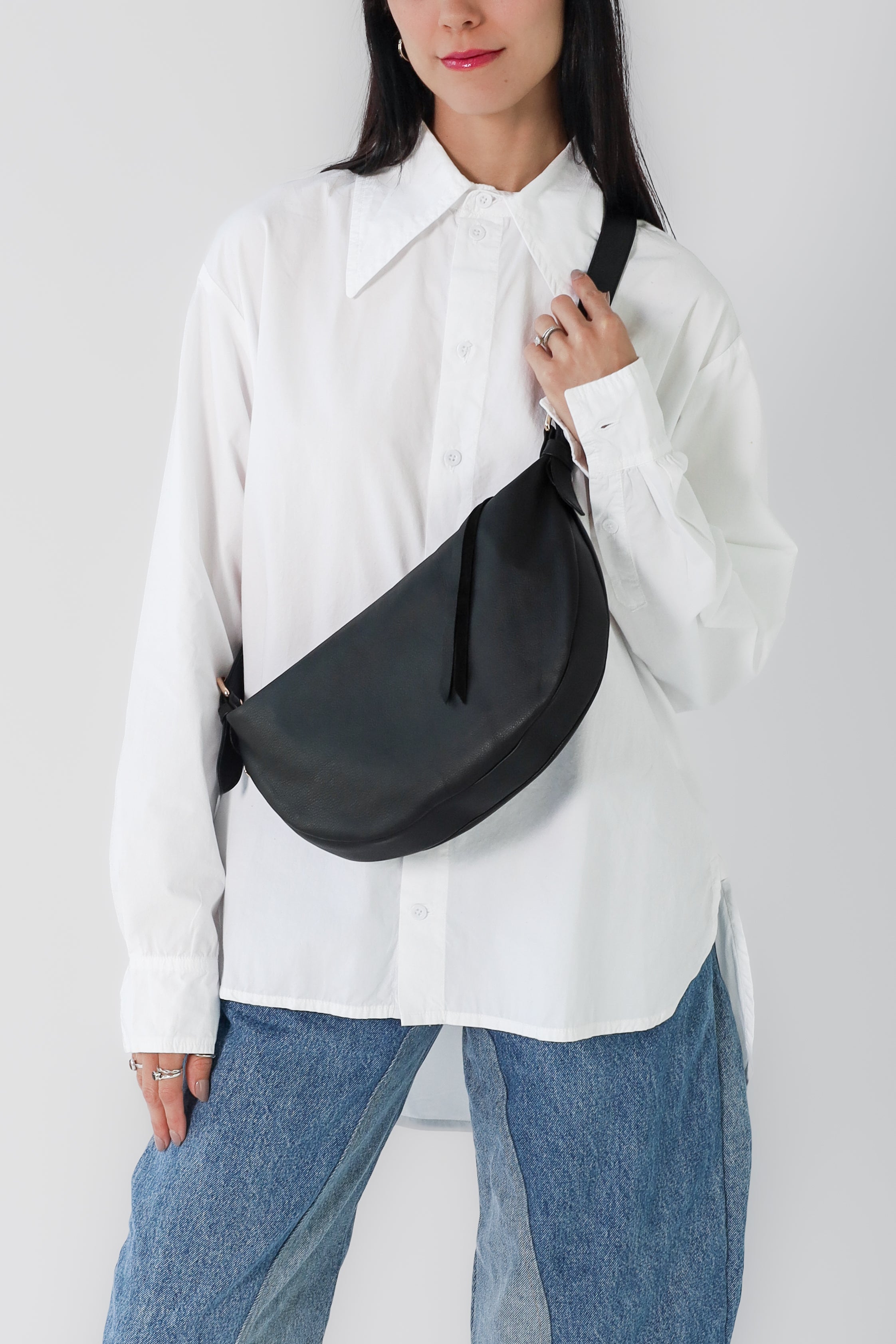 Nova Sling Bag in full-grain leather with brass hardware, softly structured curved silhouette, zipper closure, interior compartments, and adjustable strap.