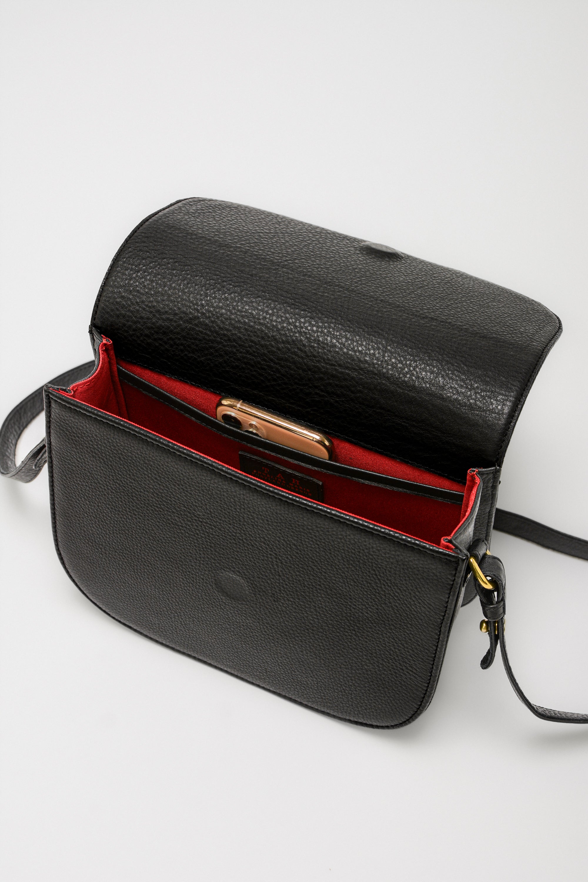 Black leather saddle handbag with red interior, showing the interior compartments