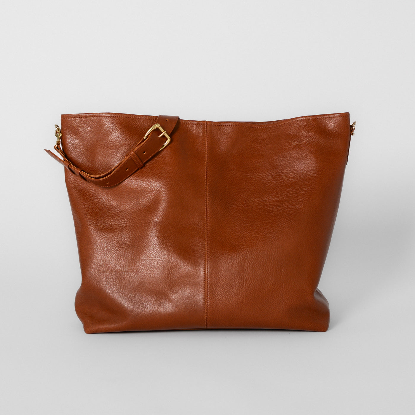 An oversized brown slouchy leather tote bag with brass hardware and an adjustable shoulder strap.