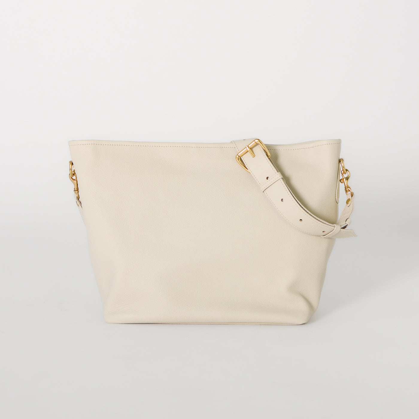 The Charlee Tote Bag in the color ivory with gold hardware details . 