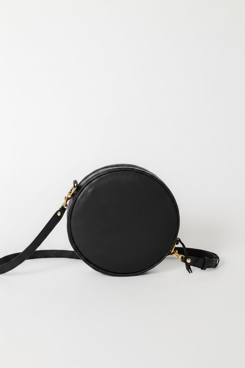 A black round crossbody bag with a black strap and small gold-tone hardware.