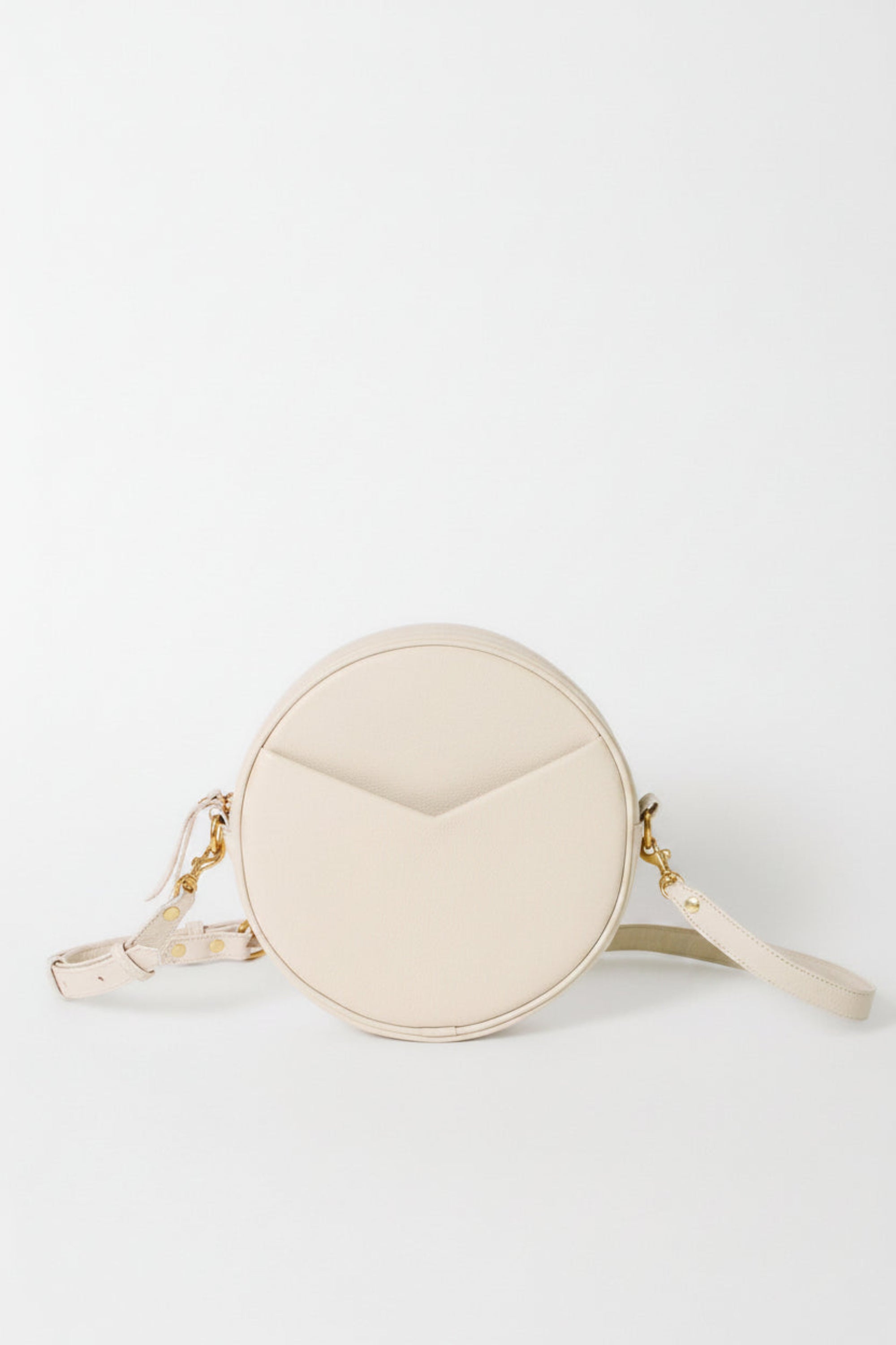 A cream-colored round crossbody bag with a geometric chevron design on the front, featuring gold-tone hardware and a matching strap
