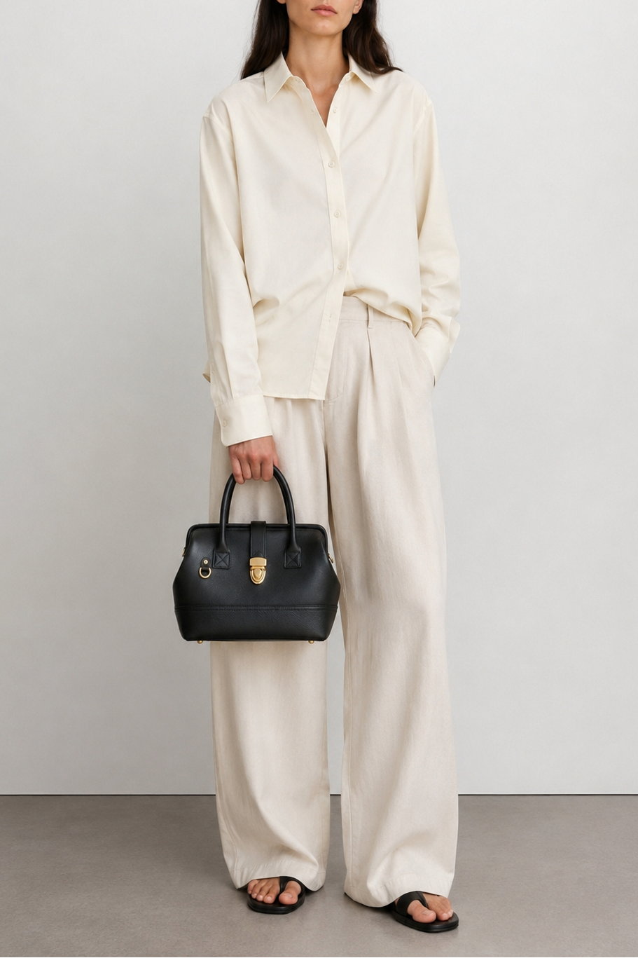Woman holding the TAH Doctor Bag in black leather, styled with an ivory blouse and wide-leg trousers.