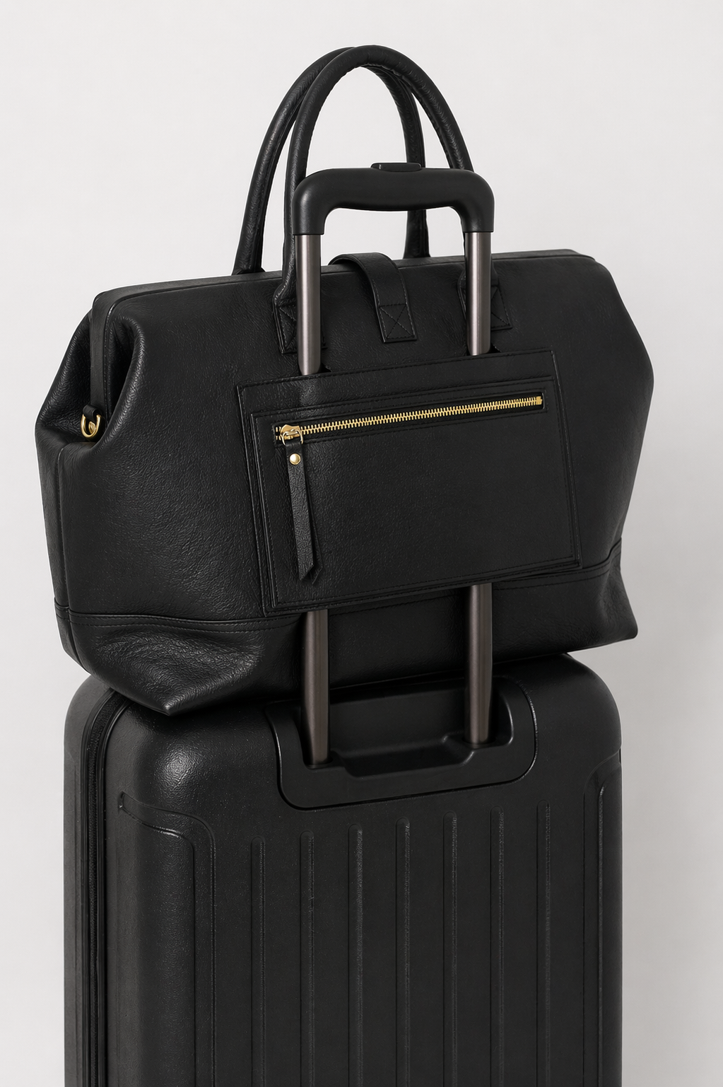 Black leather Doctor Weekender bag on top of a black suitcase showing the use of the luggage pass-through pocket