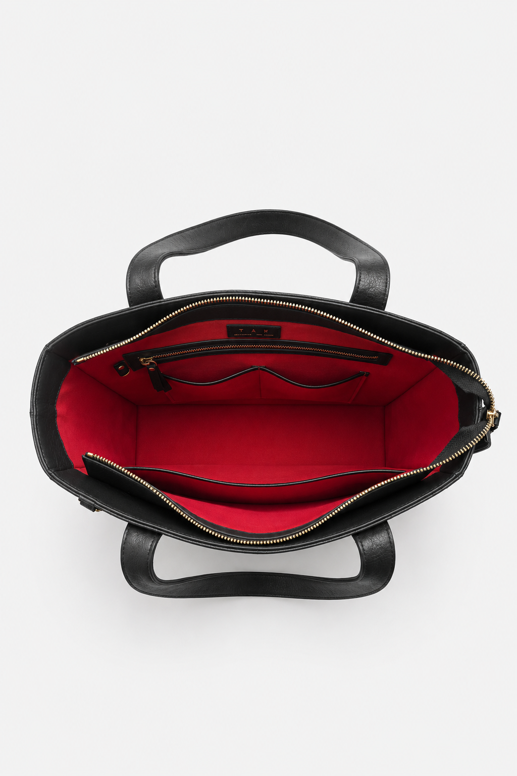 Top-down view of a black leather handbag with a bright red interior lining, featuring dual top handles and a zippered compartment.