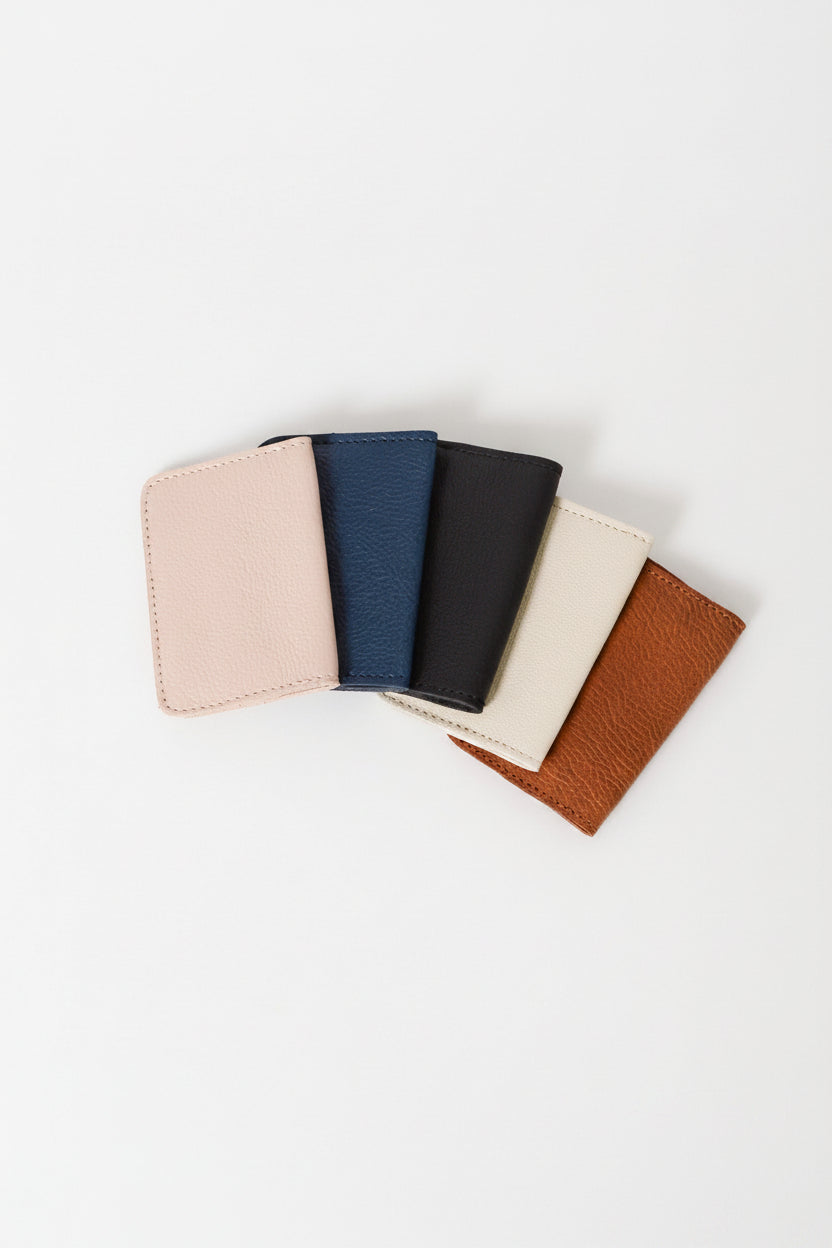 A collection of foldover wallets in various colors including pink, blue, black, beige, and brown, displayed in a fanned arrangement on a white background.