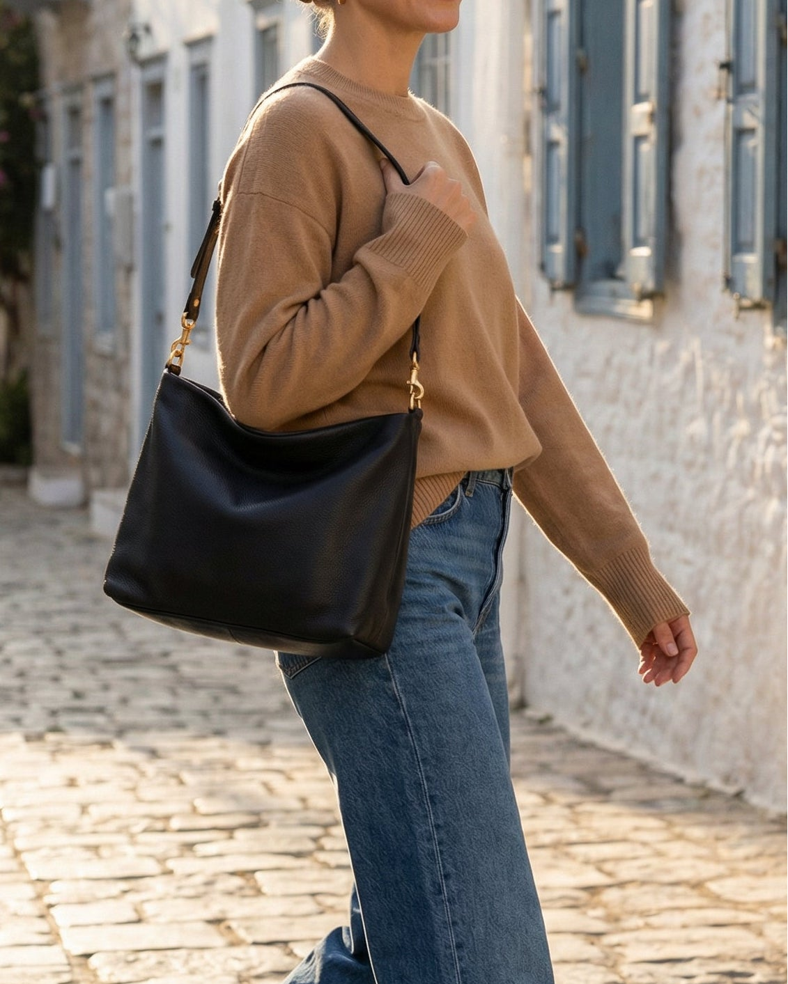 Woman walking down a sunlit street carrying a black bag