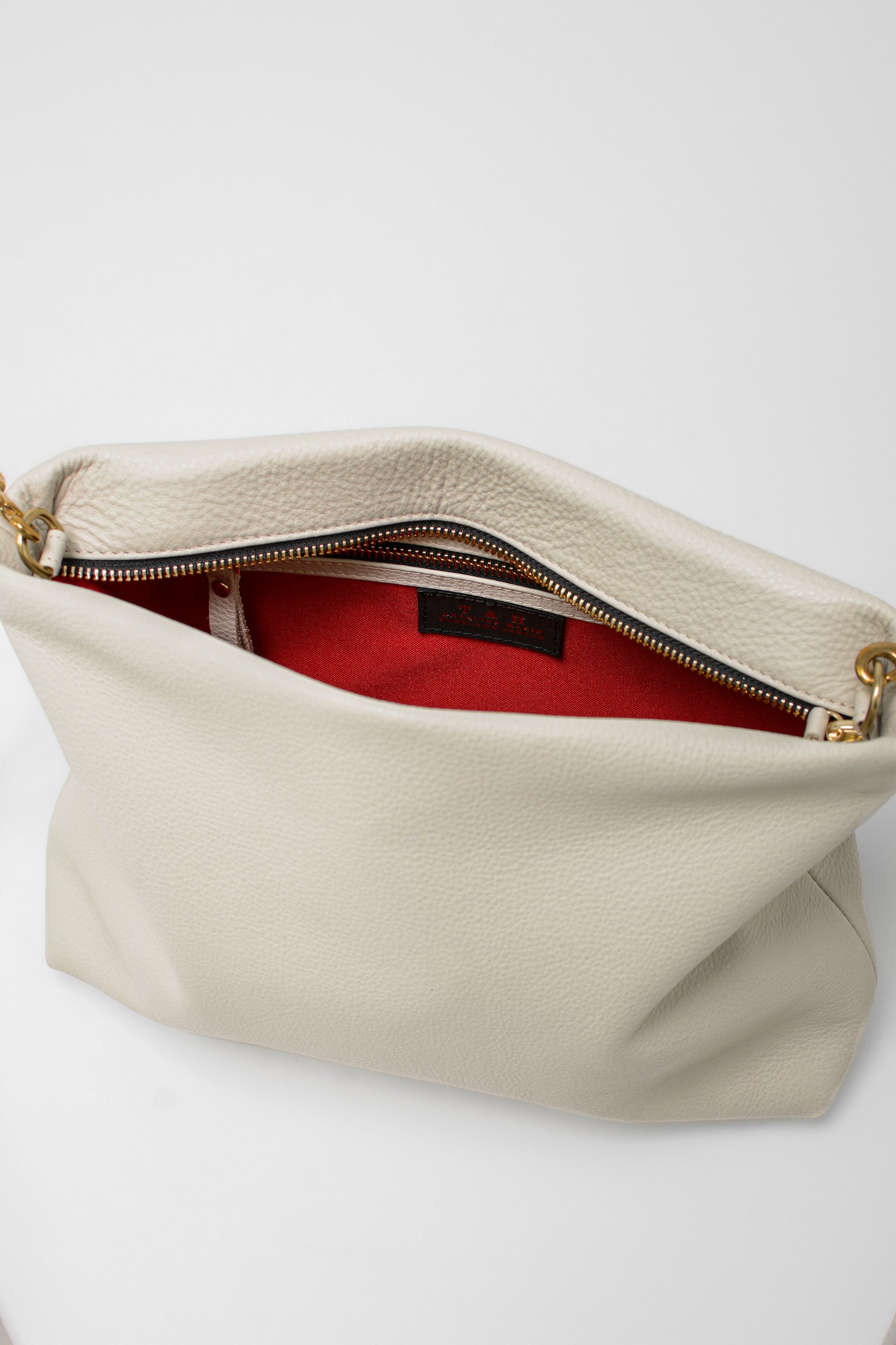 Off-white leather handbag with gold zipper on a white background showing red lining