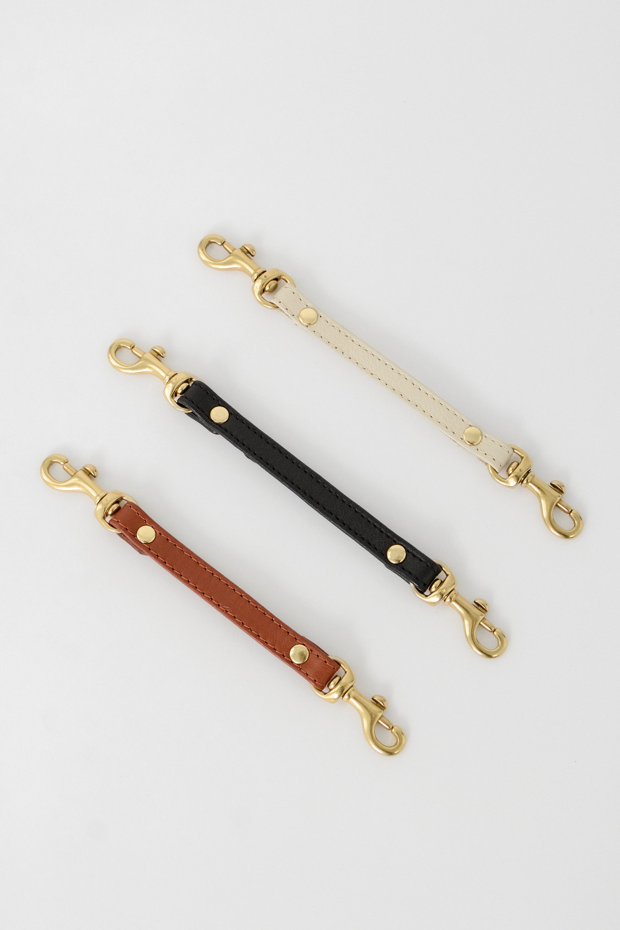 Three leather straps to attach to your keys or handbag with gold hardware on a light gray background