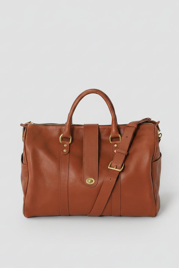 Loen Weekender Duffle in brown leather with two handles, a shoulder strap, and solid brass hardware. 