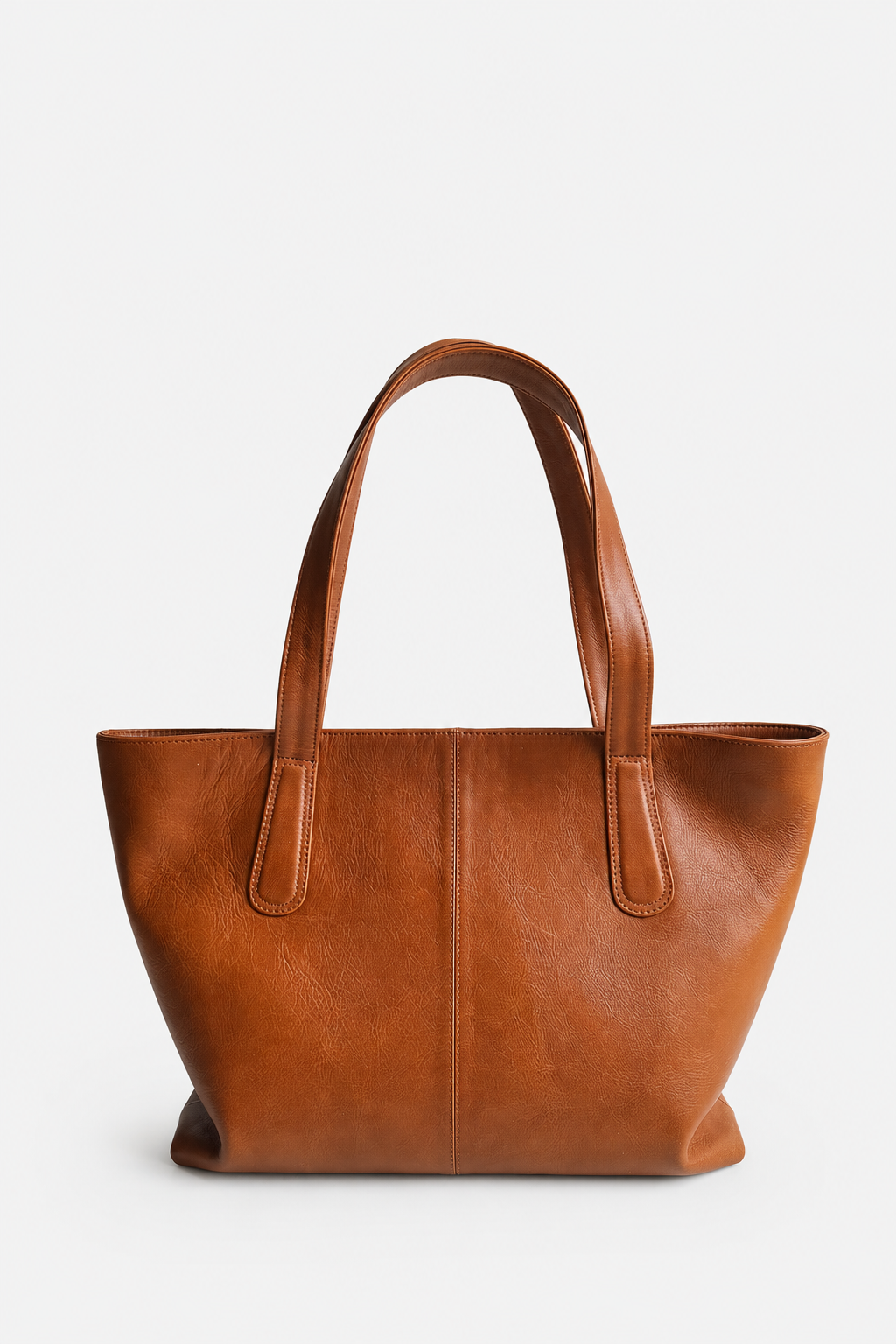 A medium brown leather tote bag with two top handles, photographed against a clean, light gray studio background. This is the Megan Everyday Tote bag in the color whiskey