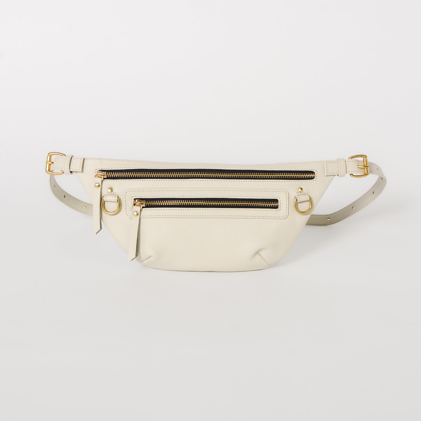 A bone leather fanny pack with brass hardware and multiple zipper compartments, displayed against a white background.