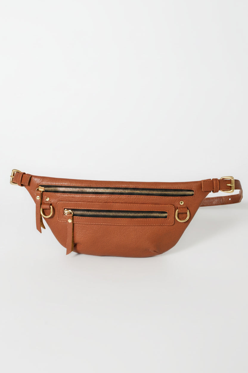Cognac leather fanny pack belt bag with adjustable strap, multiple zip pockets, and gold hardware, designed as a hands-free everyday bag for travel, errands, and daily essentials.