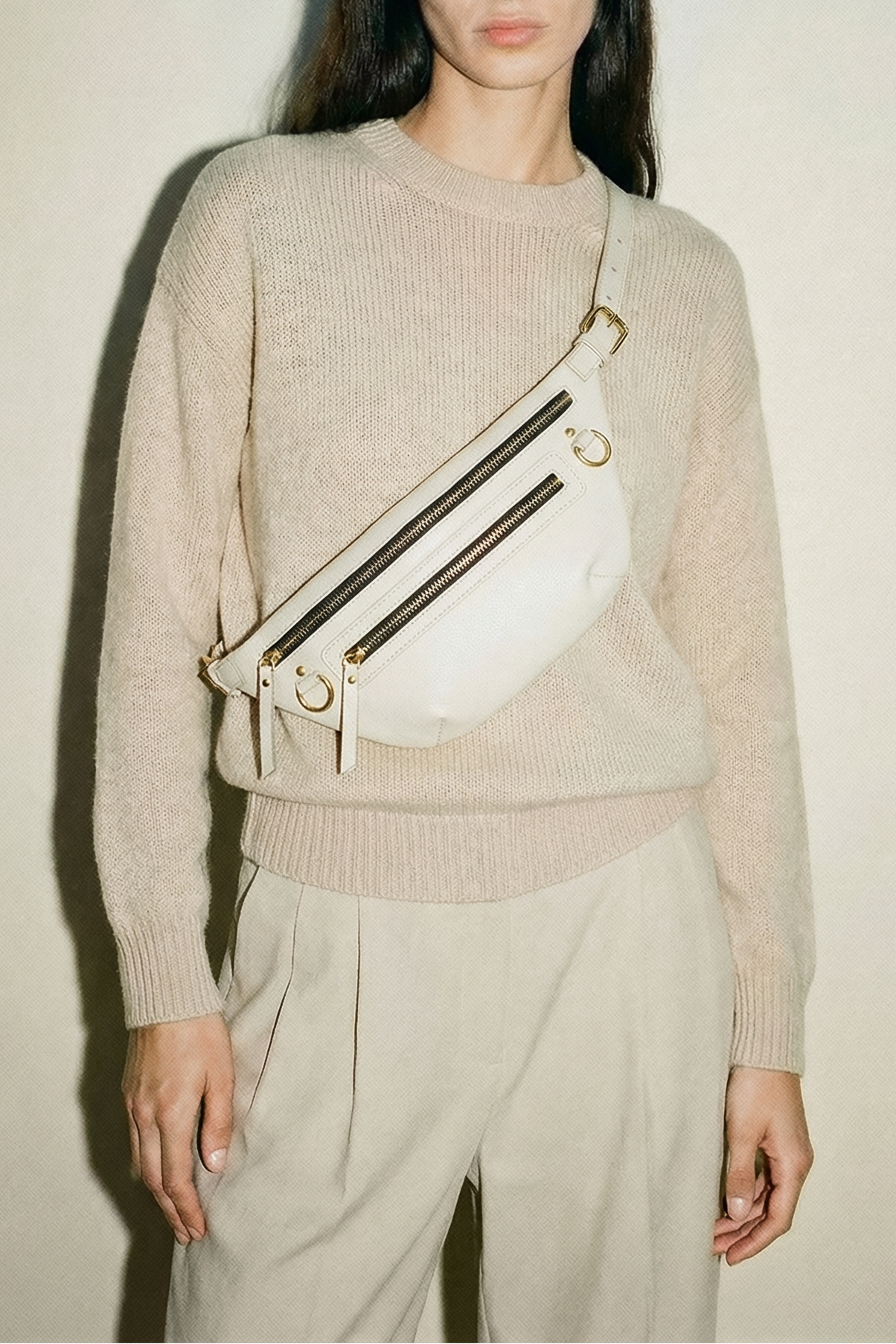 White leather fanny pack belt bag worn crossbody, featuring an adjustable strap, multiple zip pockets, and gold hardware, designed as a refined, hands-free everyday bag for travel, errands, and daily essentials.