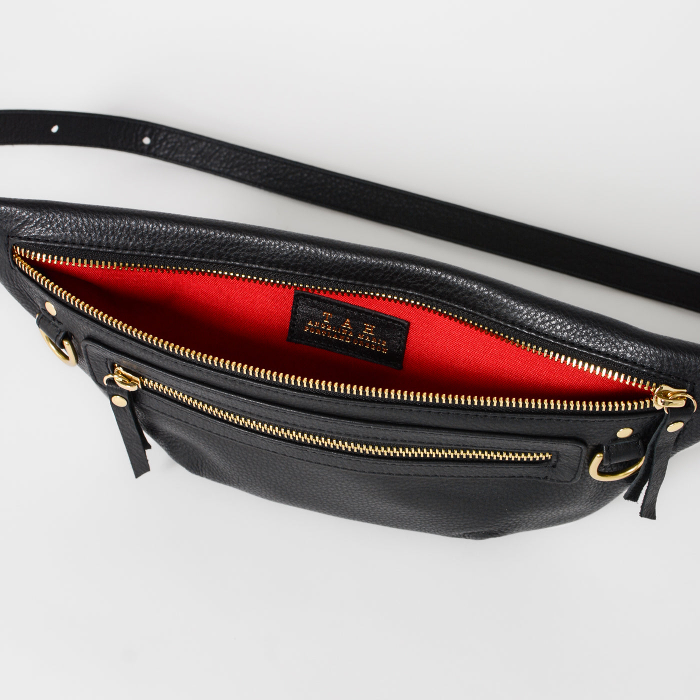 Black leather fanny pack belt bag interior with red lining, featuring zip pockets and organized compartments, designed for easy access to everyday essentials and travel items.
