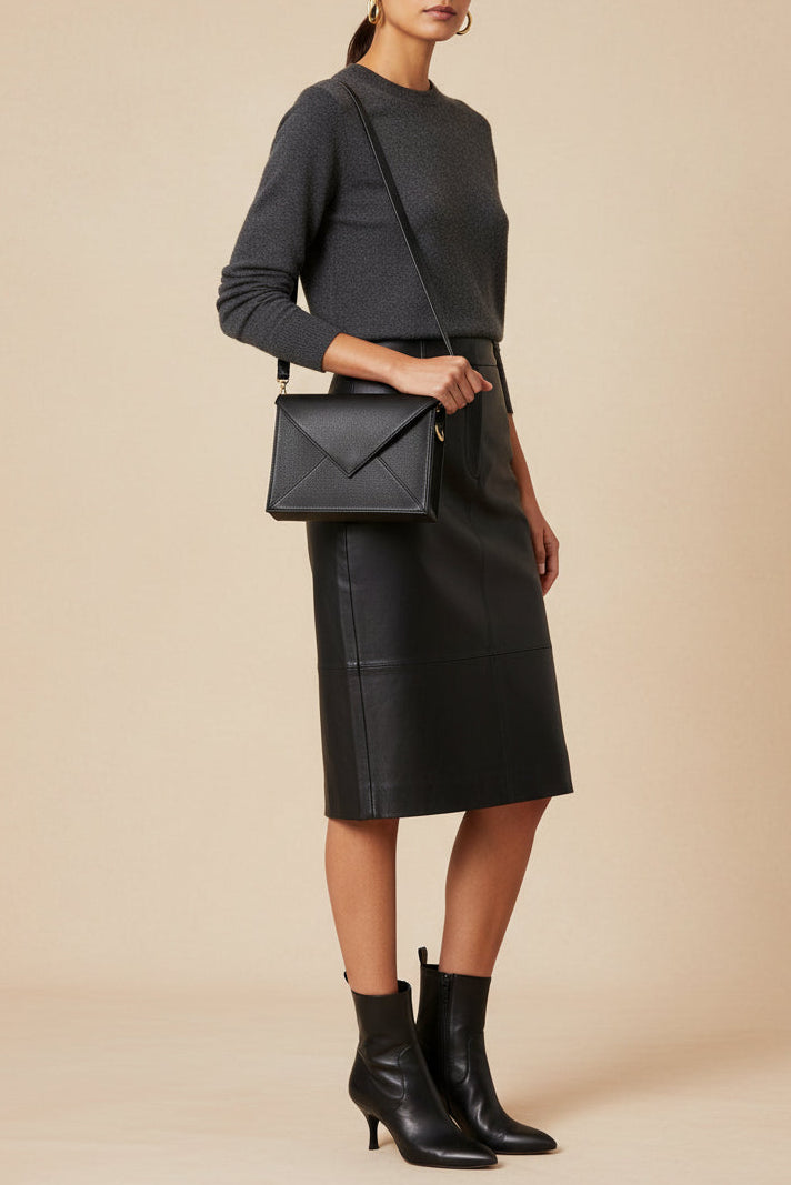 Woman wearing a black outfit with a leather skirt and carrying a matching handbag on a beige background