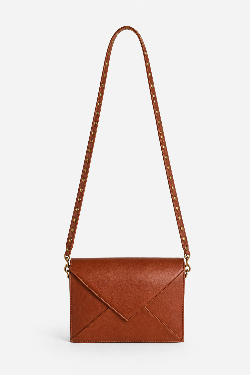 A brown leather crossbody bag with an envelope-style front flap and a long shoulder strap adorned with small gold studs, shown against a plain light gray background. This is the Nora Crossbody.