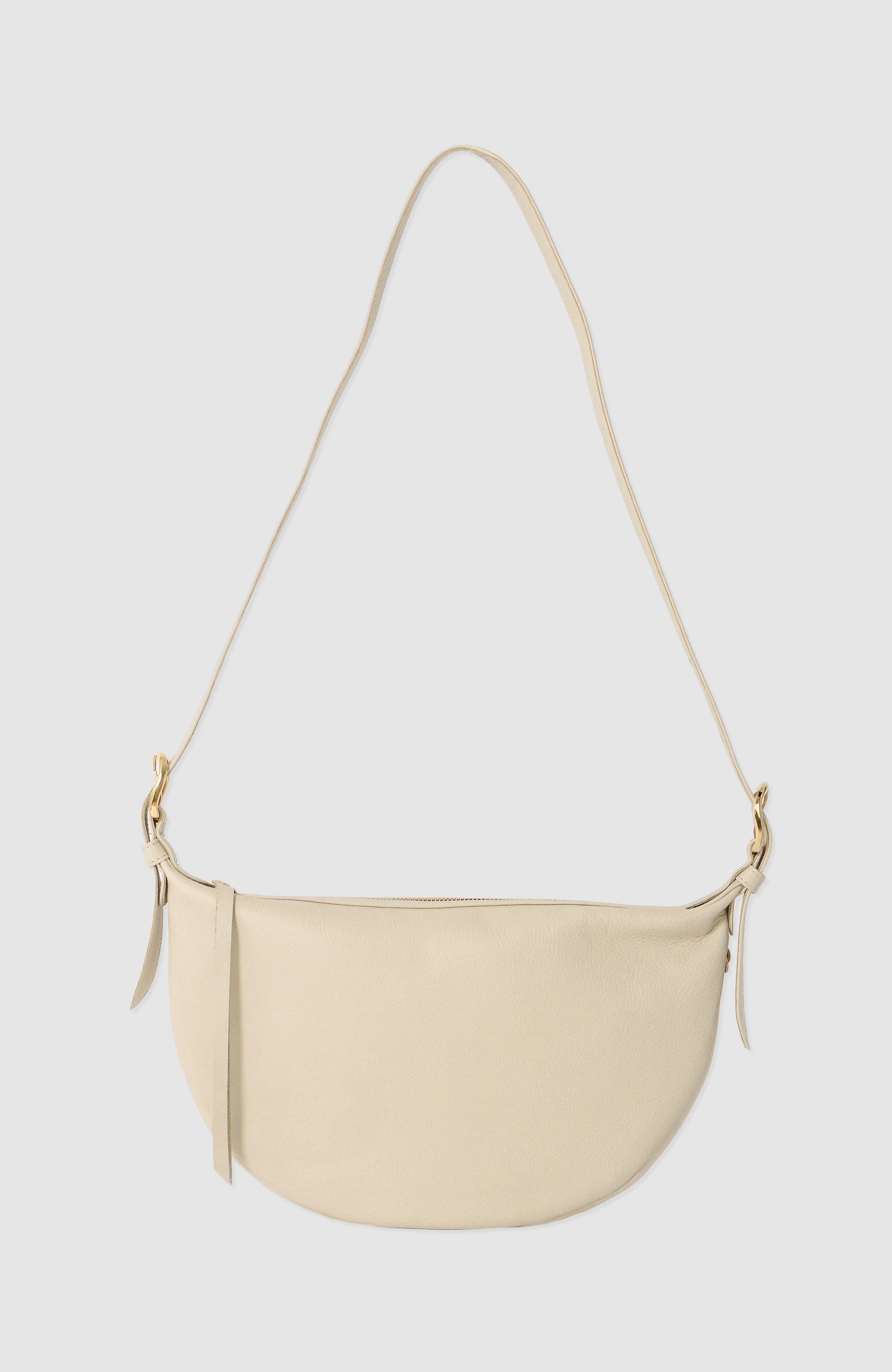 Nova Sling Bag in full-grain leather with brass hardware, softly structured curved silhouette, zipper closure, interior compartments, and adjustable strap.