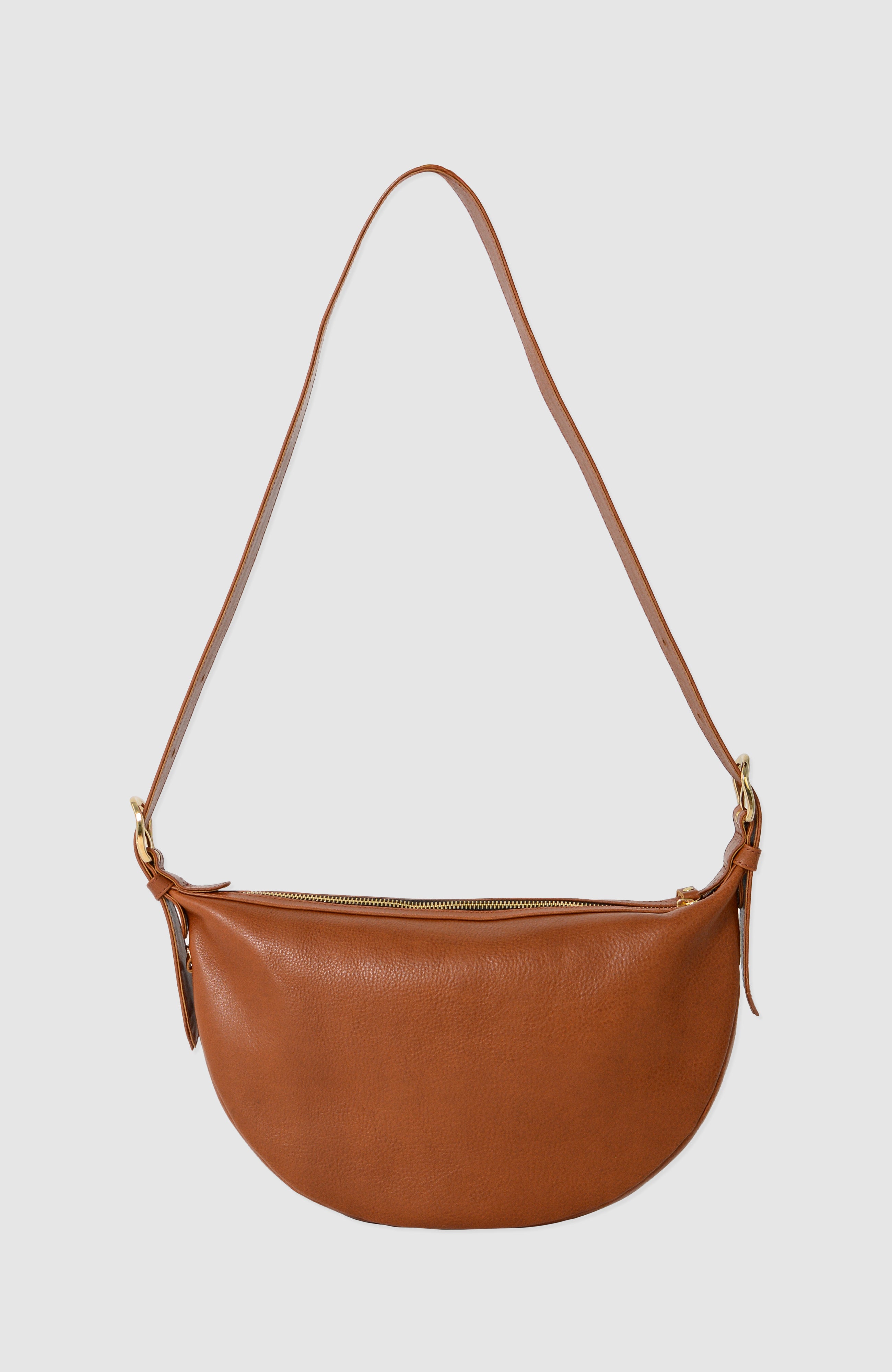 Nova Sling Bag in full-grain leather with brass hardware, softly structured curved silhouette, zipper closure, interior compartments, and adjustable strap.
