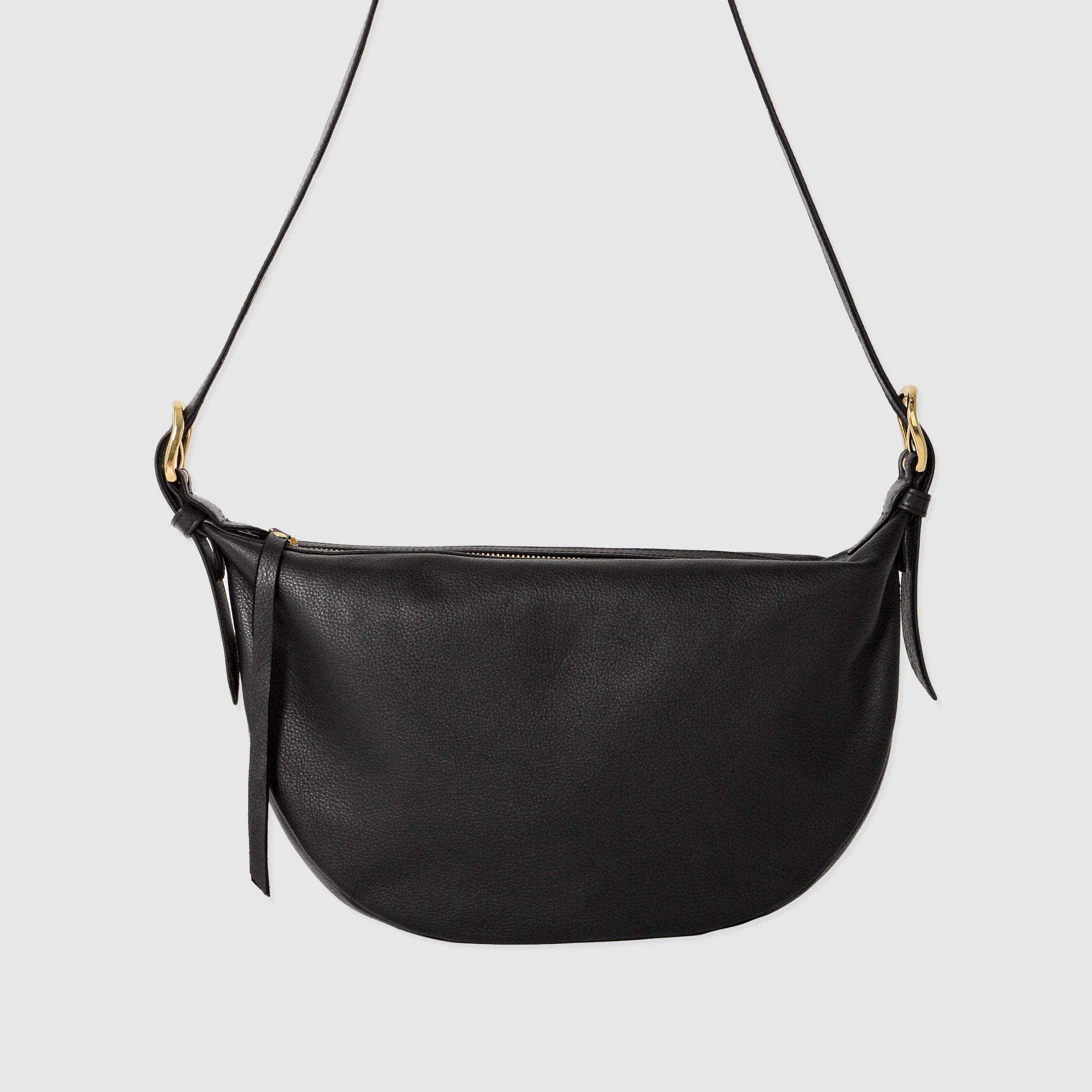 Nova Sling Bag in full-grain leather with brass hardware, softly structured curved silhouette, zipper closure, interior compartments, and adjustable strap.