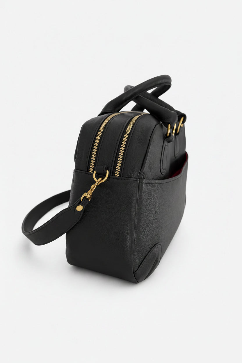 A black leather handbag with a top handle, a detachable shoulder strap, and gold-tone hardware, shown from a three-quarters angle on a light gray background.