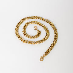 A coiled gold-colored Cuban chain bag strap with bolt swivel clasps on a white background.