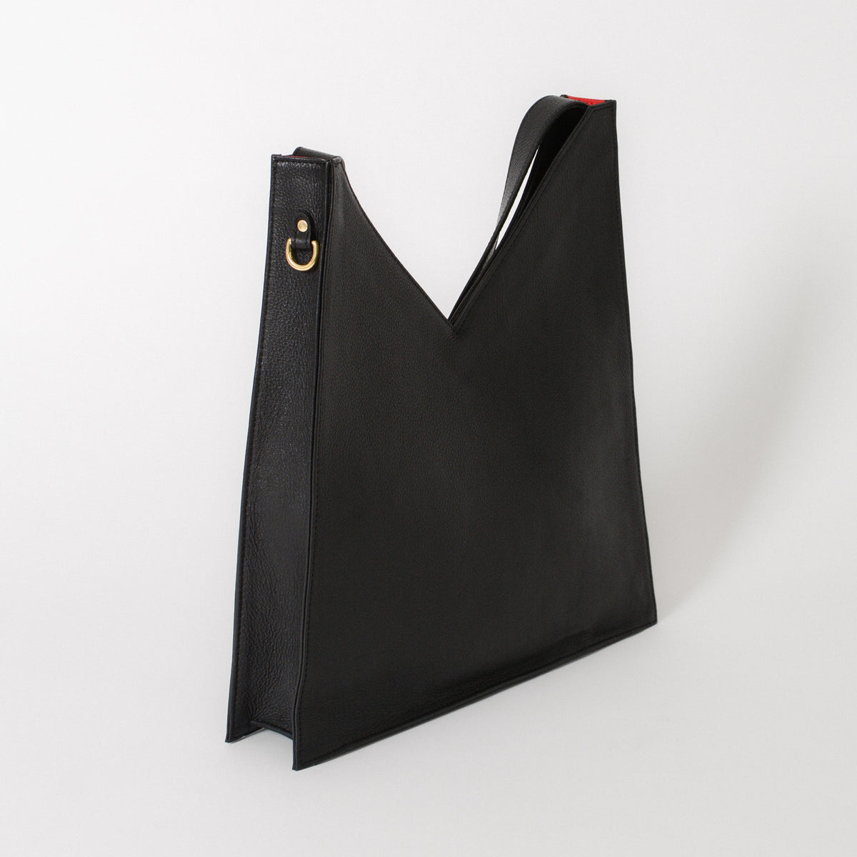A black leather tote bag showing the side view with a gold d ring on the side.