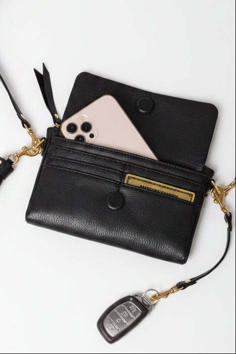 A black pebbled leather crossbody wallet with a solid brass key link strap and key fob, shown open with a phone tucked inside and six credit card slots. 