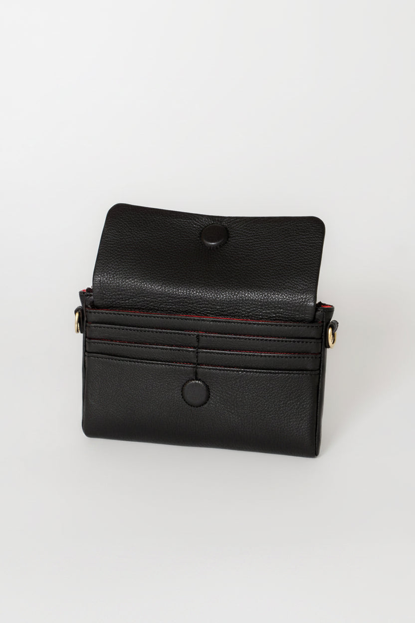 A black pebbled leather crossbody bag with a flap closure, featuring a snap button, card slots, and a thin red accent line along the edge, shown on a light gray background.