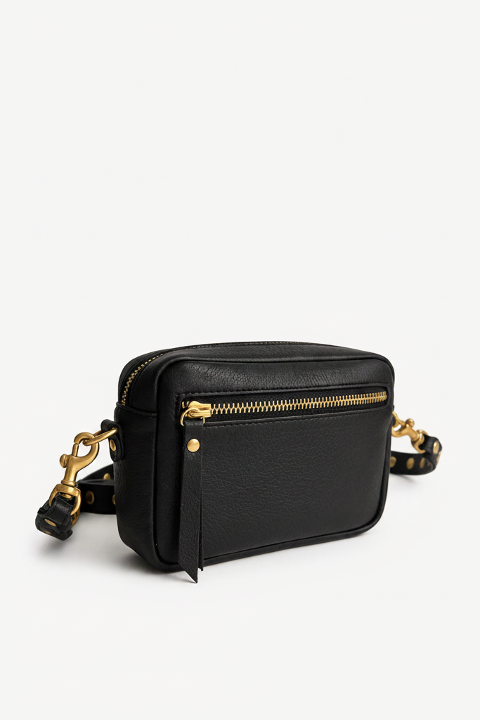 Compact black leather Ami Crossbody bag featuring a back zip pocket, gold hardware, and an adjustable studded strap for hands-free wear.