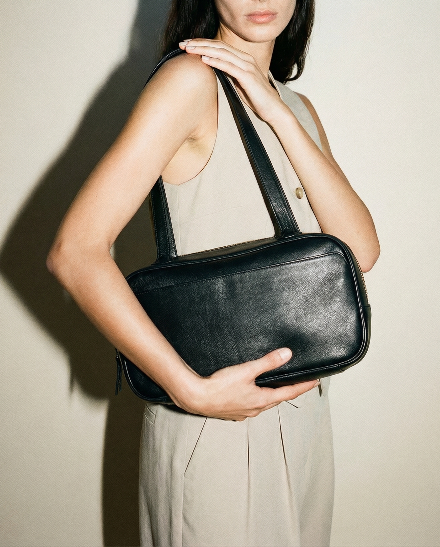 Black leather shoulder bag worn on shoulder, featuring a structured rectangular silhouette, long straps, and top zip closure, styled as a minimalist everyday bag for work, travel, and elevated daily wear.