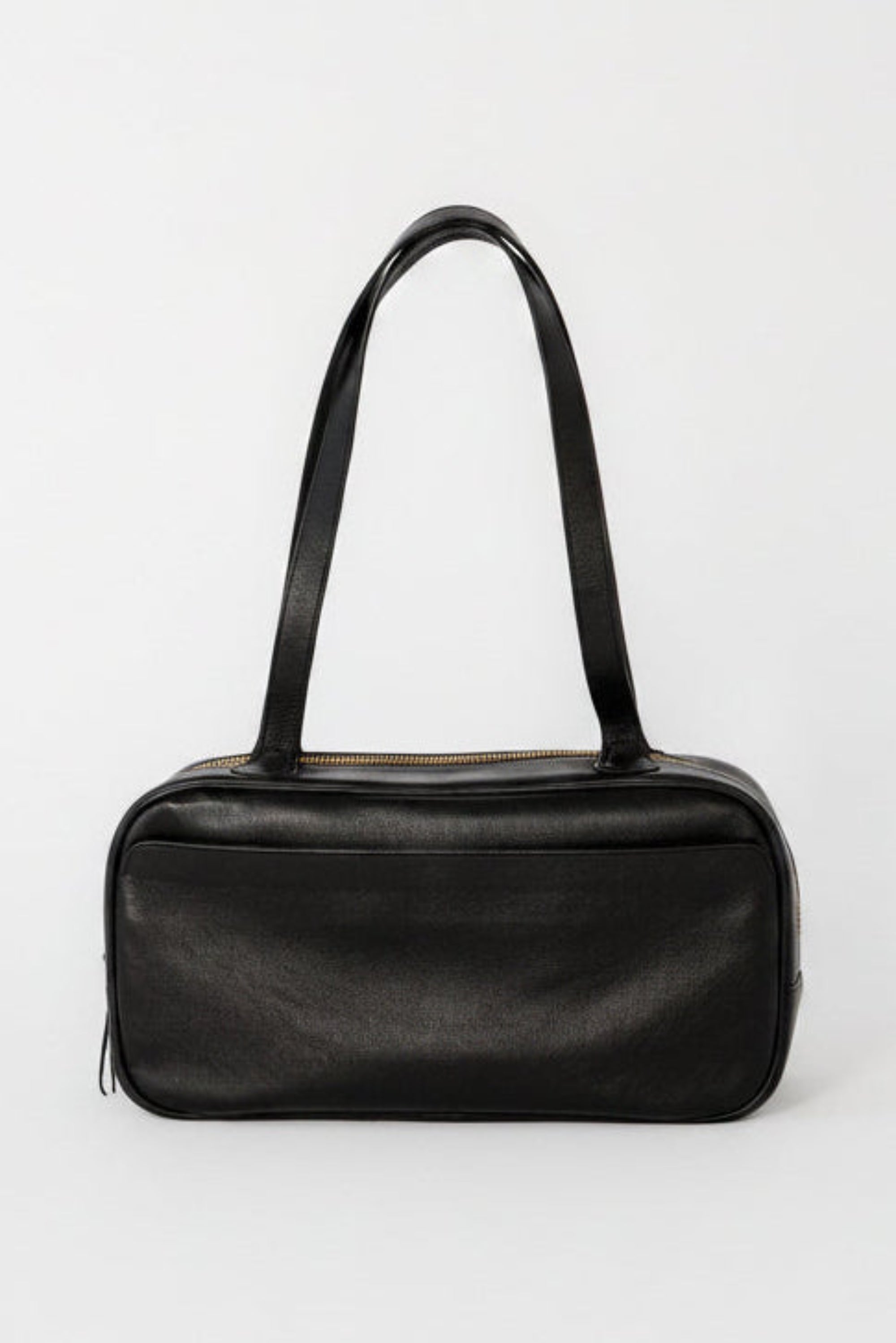 Black leather bowler shoulder bag with a structured rectangular silhouette, long straps, and top zip closure, designed as a minimalist everyday bag for work, travel, and daily use.