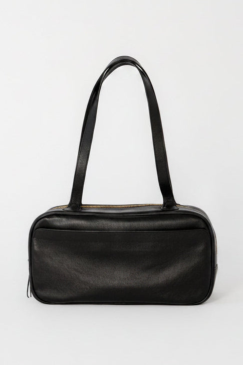 Black leather bowler shoulder bag with a structured rectangular silhouette, long straps, and top zip closure, designed as a minimalist everyday bag for work, travel, and daily use.