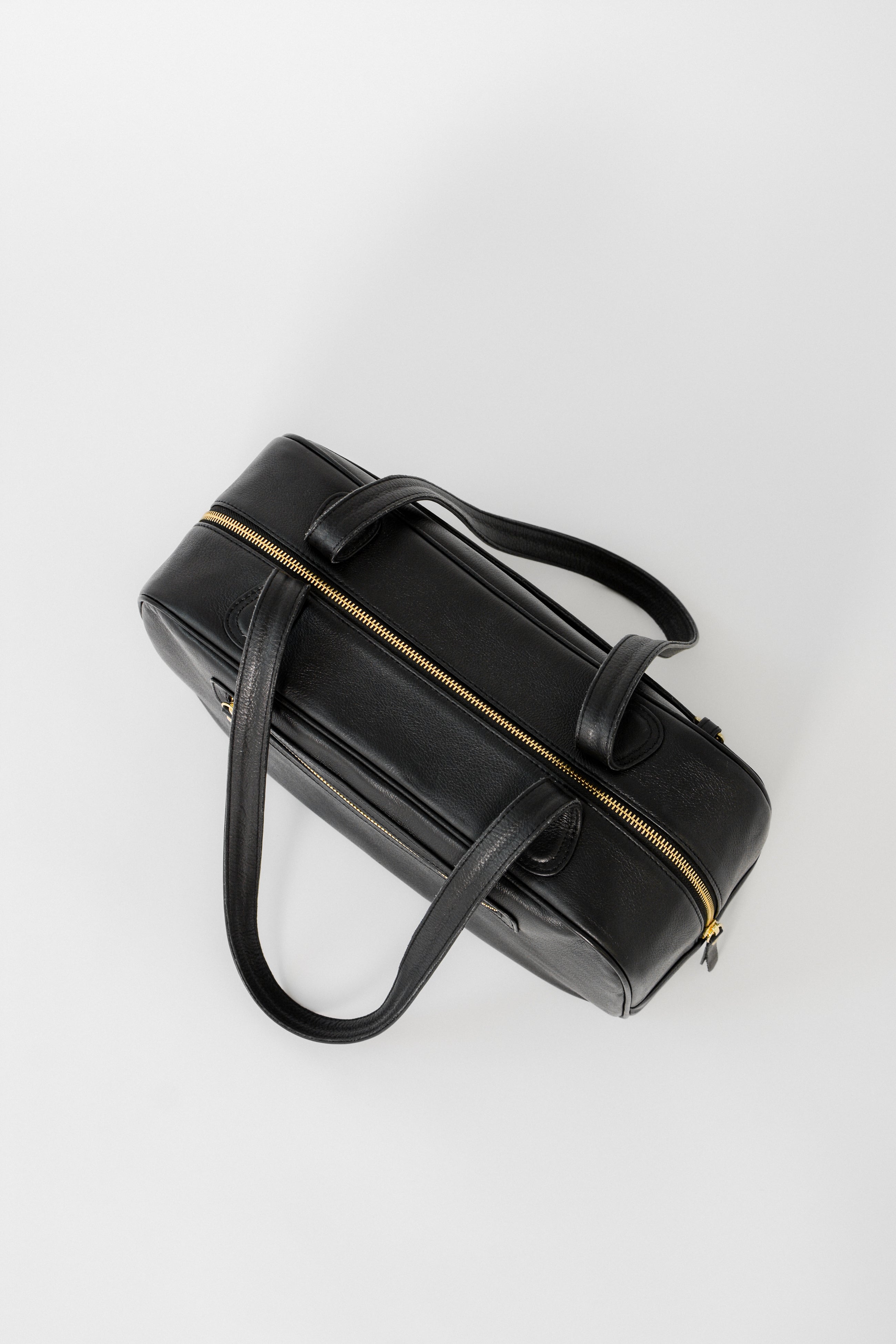 Black leather shoulder bag with a structured rectangular shape, shown from a top angled view, highlighting the full zip closure, long straps, and streamlined design for everyday work or travel.