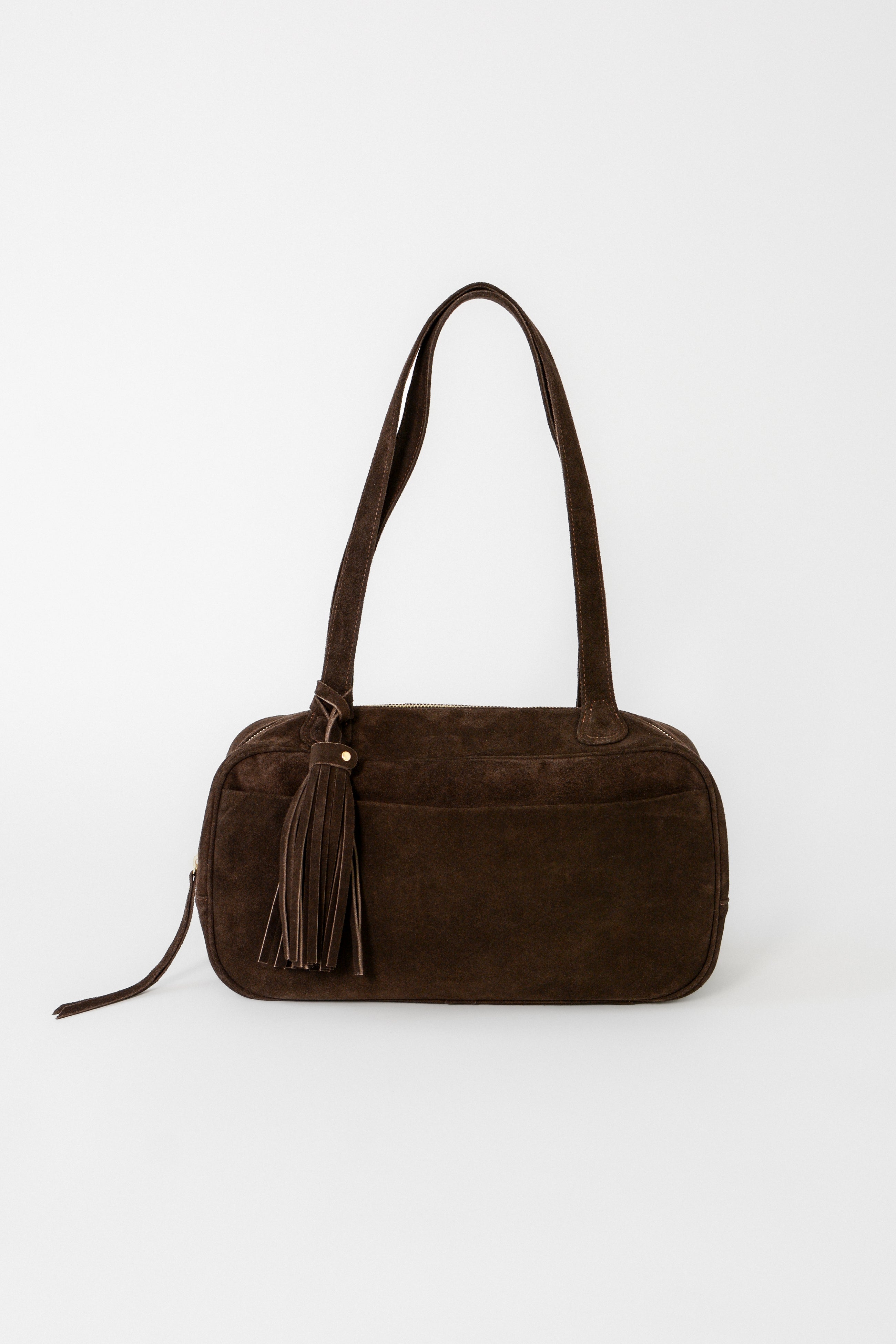 Chocolate brown suede leather shoulder bag with a structured rectangular silhouette, long straps, top zip closure, and tassel detail, designed as a minimalist everyday bag for work or travel.