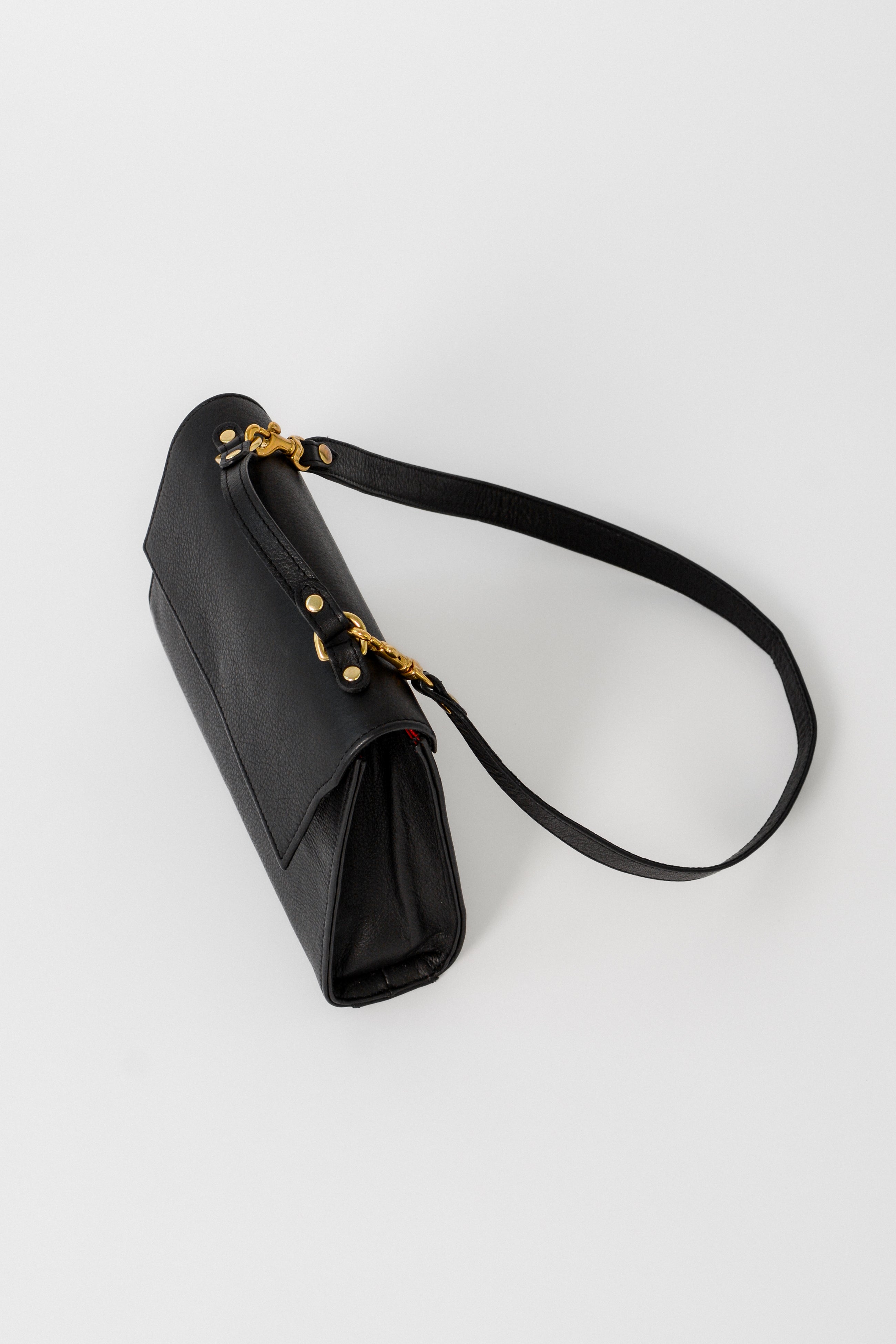 Side view of the black leather Carrie Petite top-handle bag with detachable strap, designed for evening wear, showcasing its structured silhouette and gold hardware details.