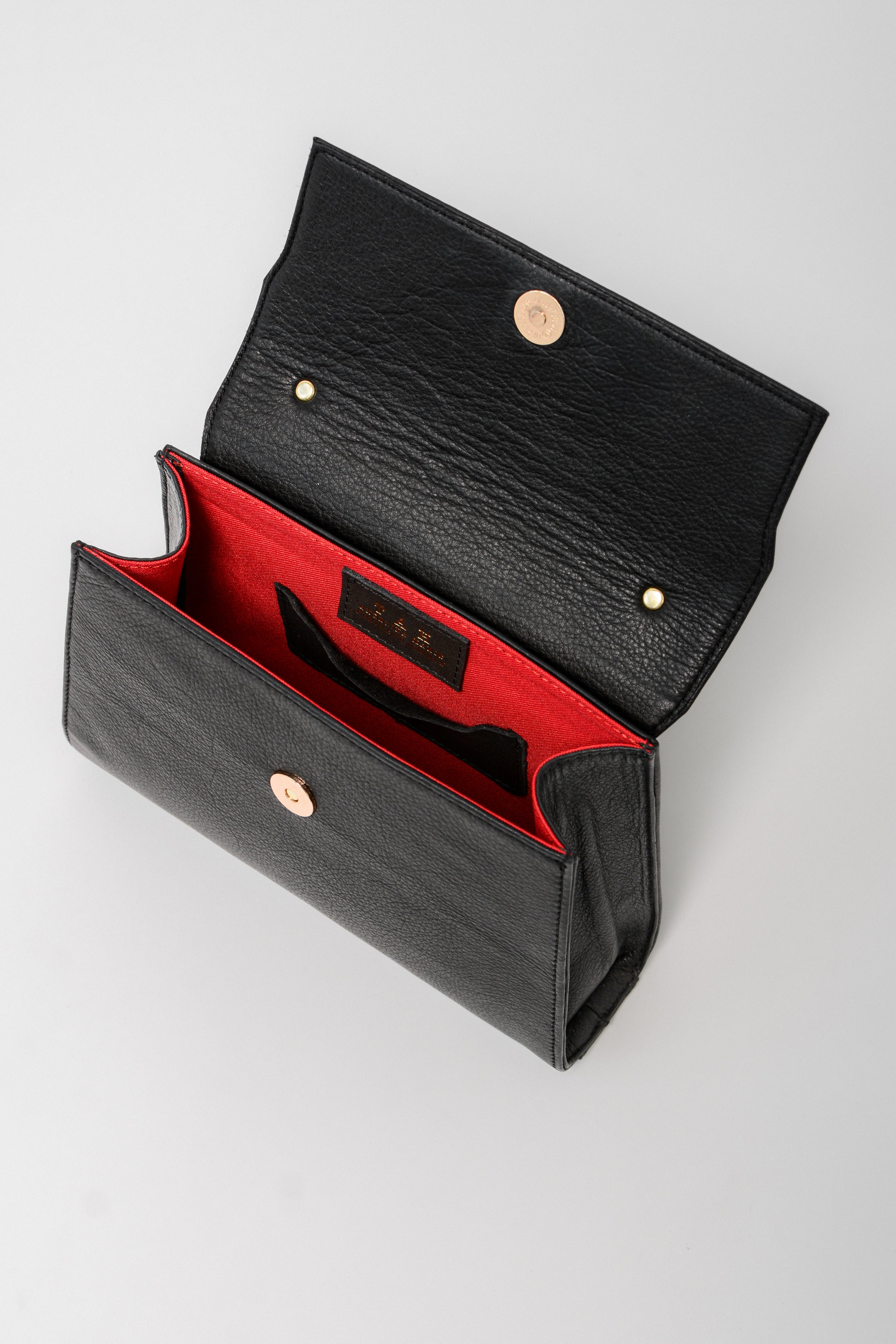 Interior view of the black leather Carrie Petite top-handle bag, featuring a bold red lining, secure snap closure, and organized compartments for essentials.