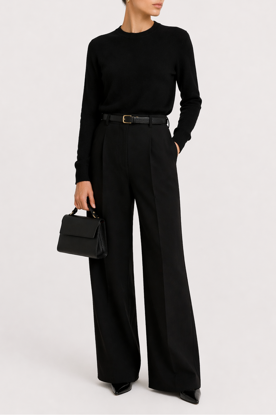 Model wearing an all-black outfit holding the Carrie Petite black leather top-handle bag, showcasing its structured shape and polished, minimal design.