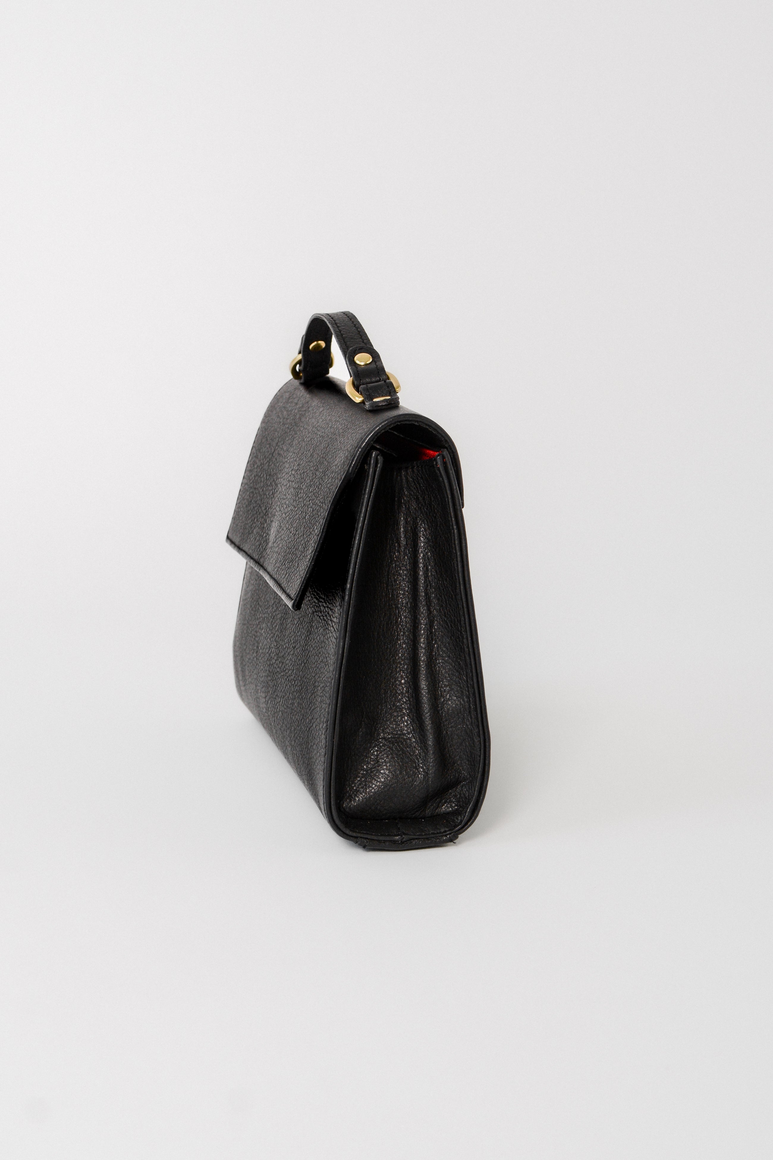 Side profile of the black leather Carrie Petite top-handle bag, highlighting its structured silhouette, gusseted sides, and compact design for polished day-to-evening use.
