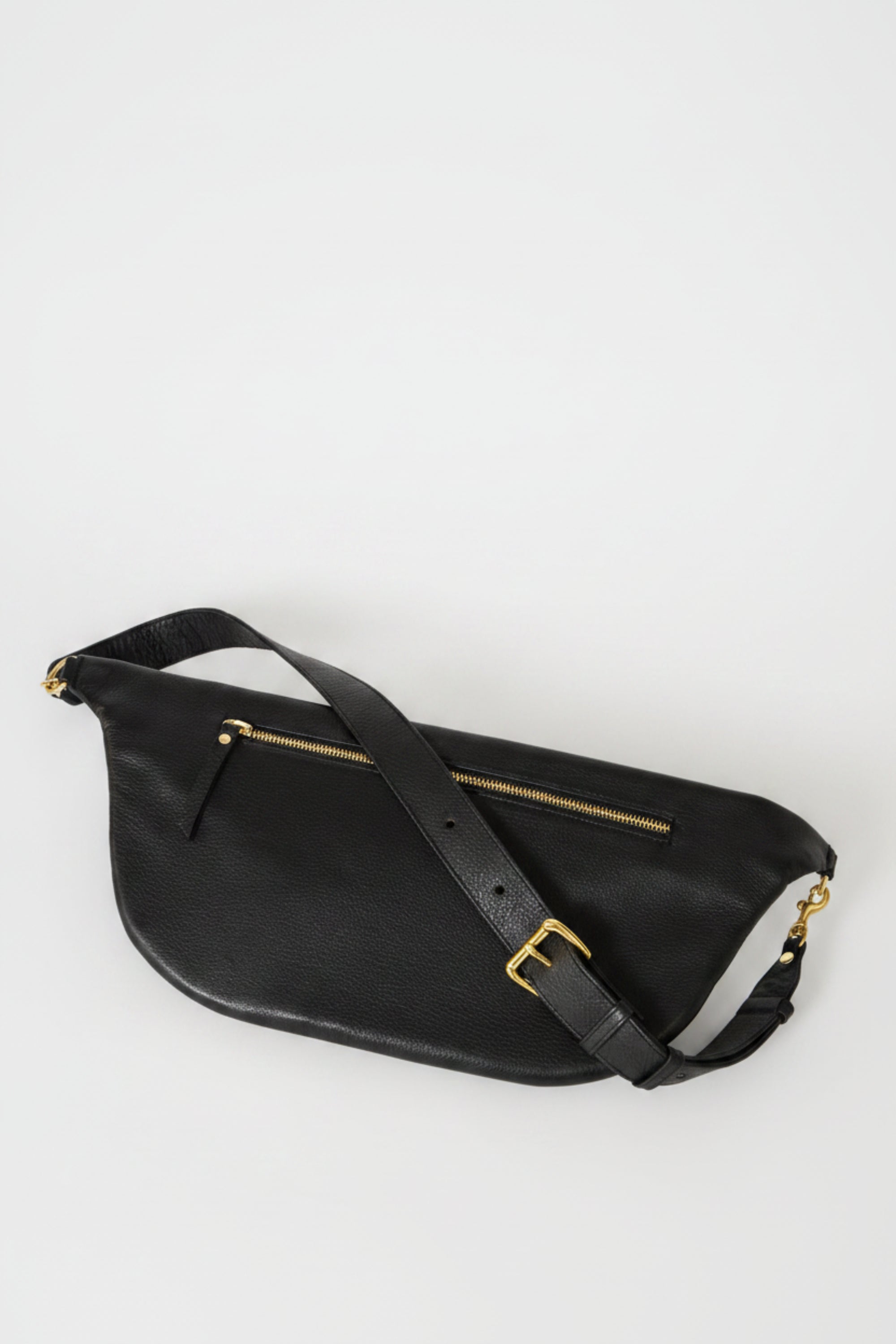 Black leather commuter sling bag shown from back angled view, featuring adjustable strap, zip pocket, and gold hardware, designed for secure, hands-free everyday use.