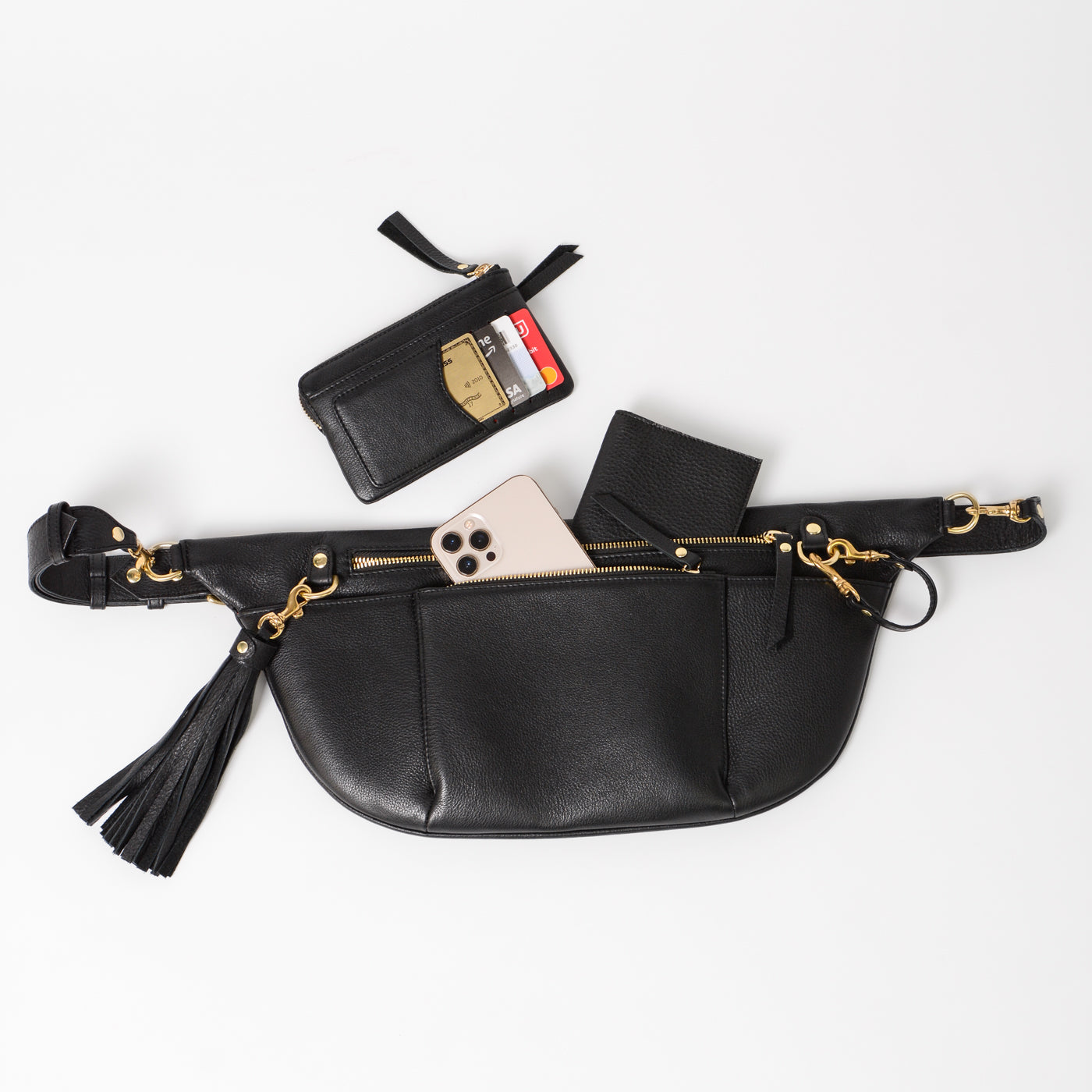 Black leather commuter sling bag with zip compartments and gold hardware, shown with phone, wallet, and card holder to highlight organized storage for everyday essentials and travel.