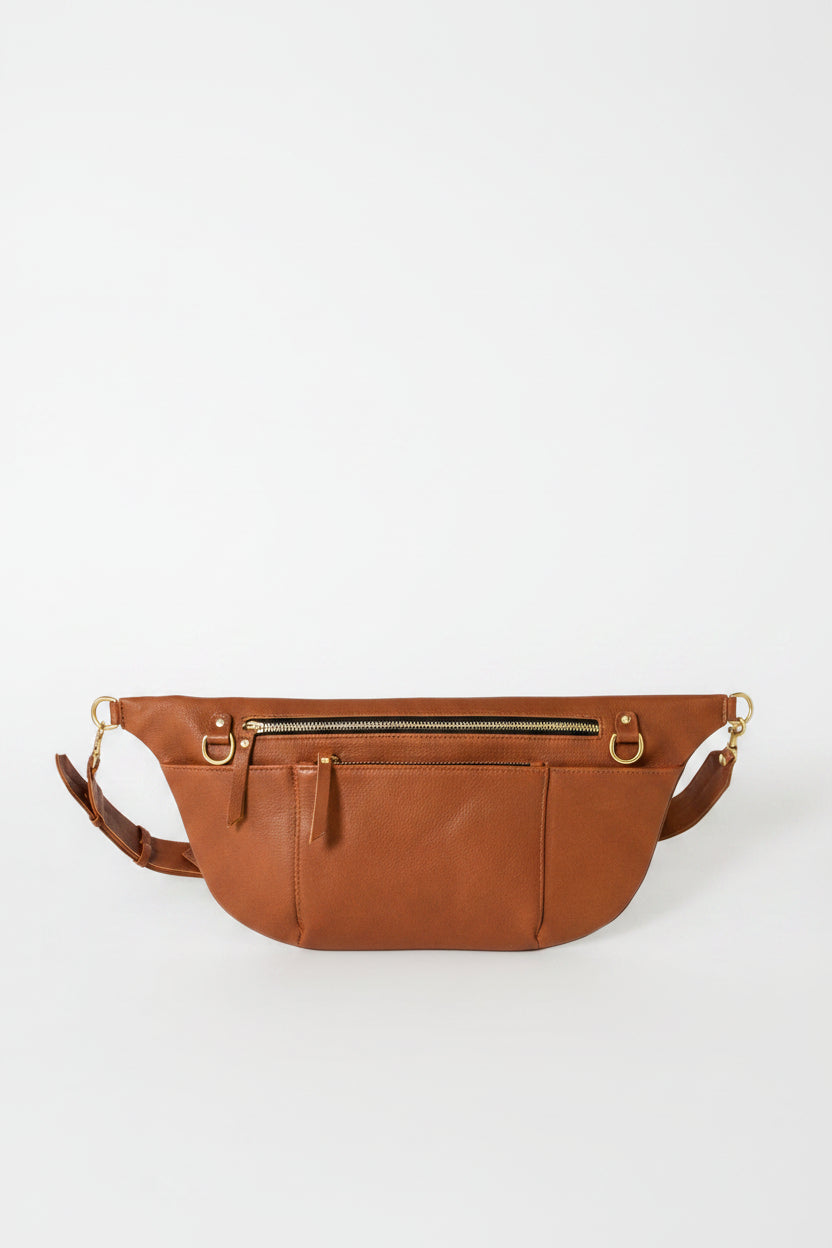Cognac leather commuter sling bag with adjustable strap, zip compartments, and gold hardware, designed as a hands-free crossbody bag for work, travel, and everyday essentials.