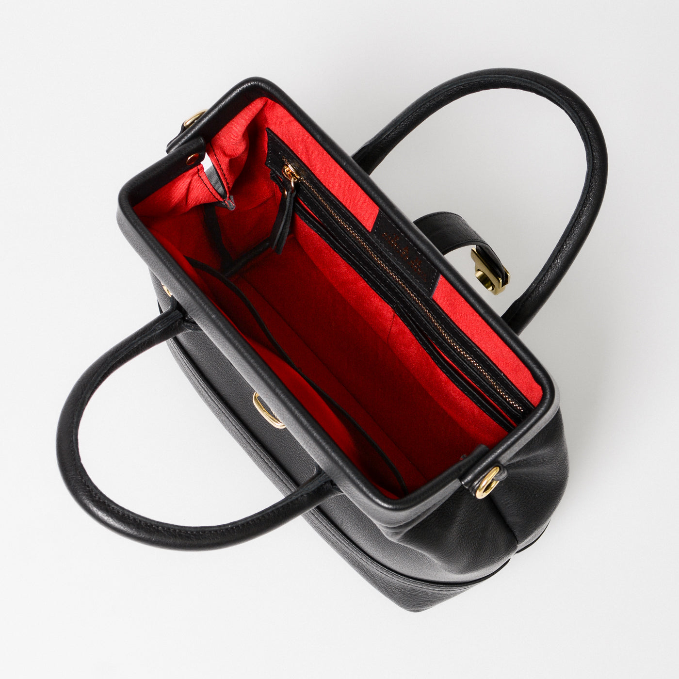 Top-down view of the Doctor Bag Petite interior, featuring a structured frame opening, red lining, zip pocket, and organized compartments.