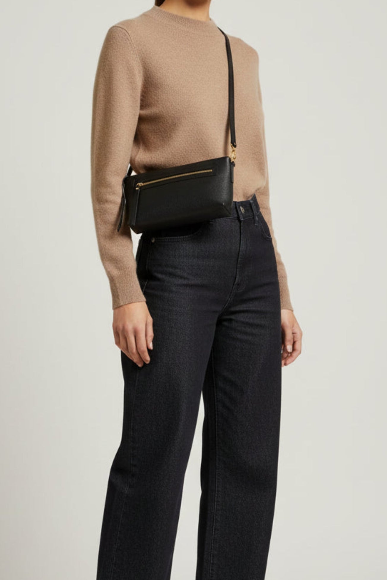 Black leather Ella shoulder bag worn crossbody on model from side view, featuring a structured silhouette, front zip pocket, and gold hardware for a streamlined everyday look.