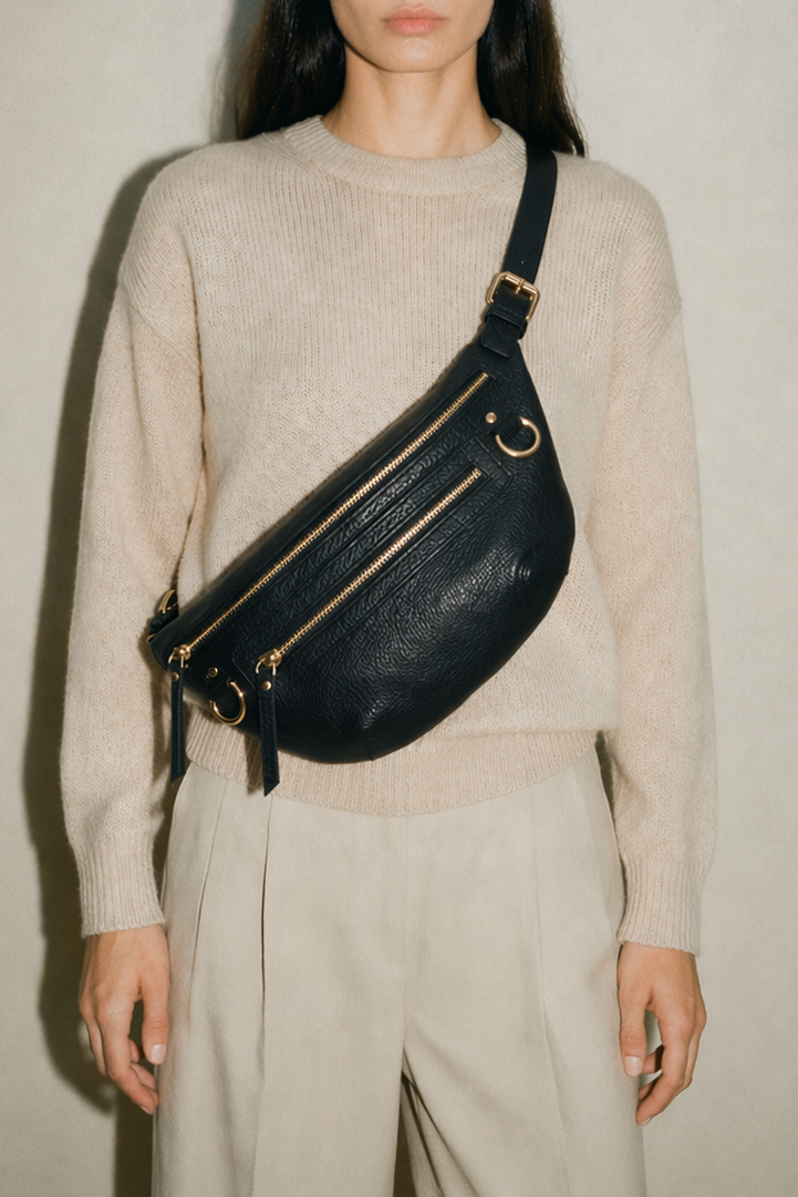 Black leather Nomad Carryall belt bag worn crossbody on model, featuring multiple zip compartments, adjustable strap, and gold hardware, designed for hands-free carry with expanded capacity for everyday essentials.