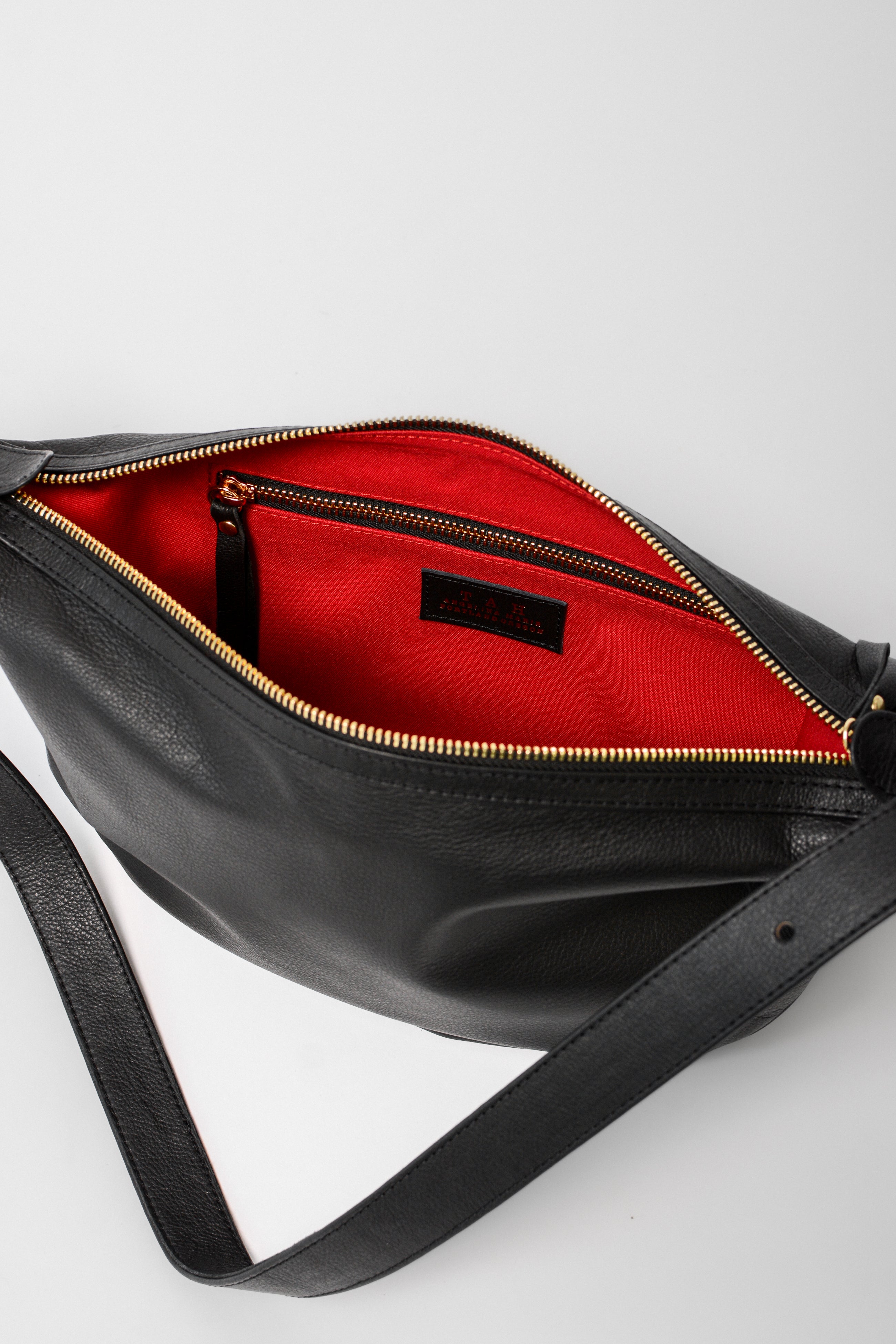 Interior of the black leather Nova Sling Bag featuring a red lining and secure zip pocket for organized everyday essentials.