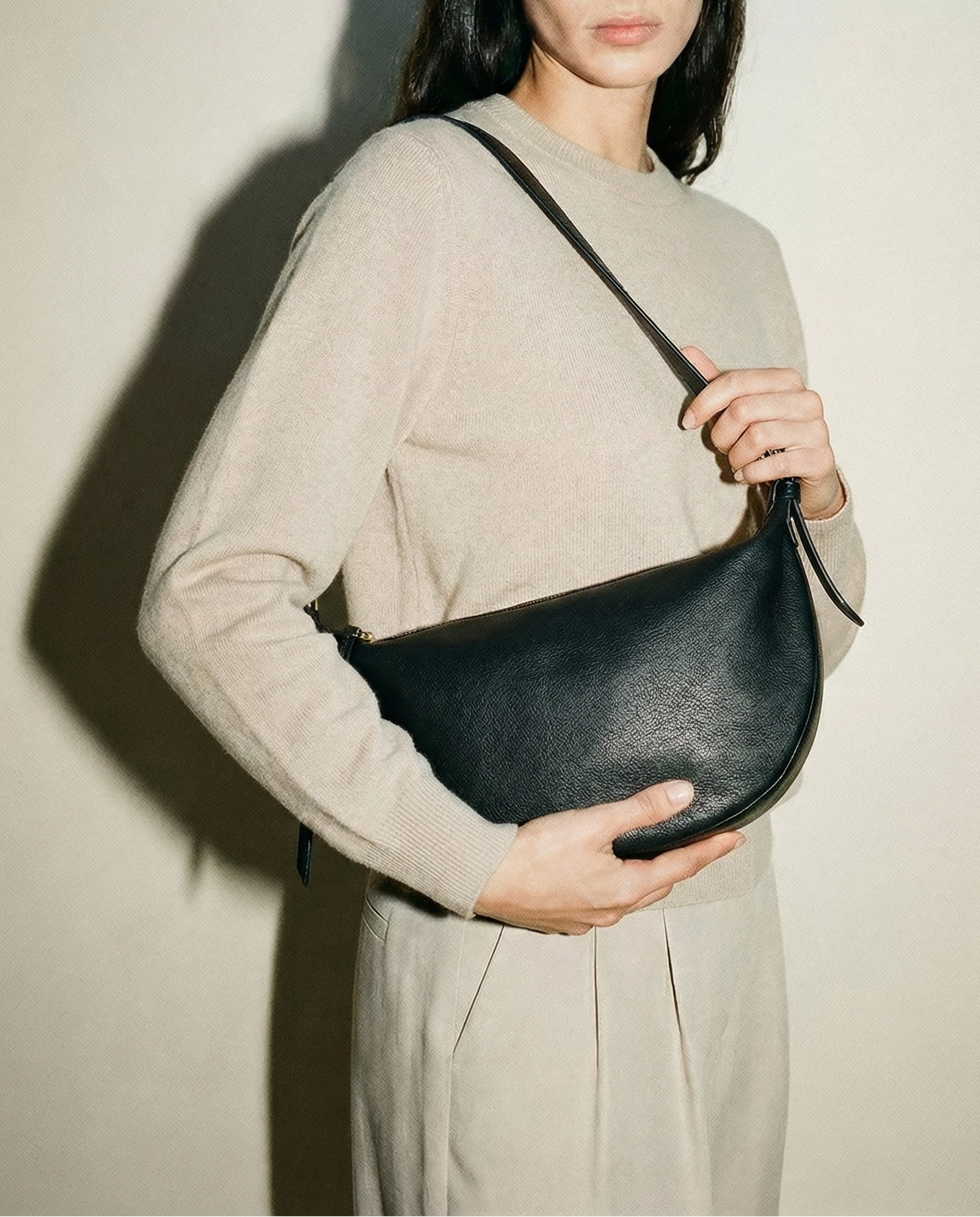 Model carrying the black leather Nova Sling Bag as a shoulder bag, showcasing its curved silhouette, soft structure, and everyday versatility.