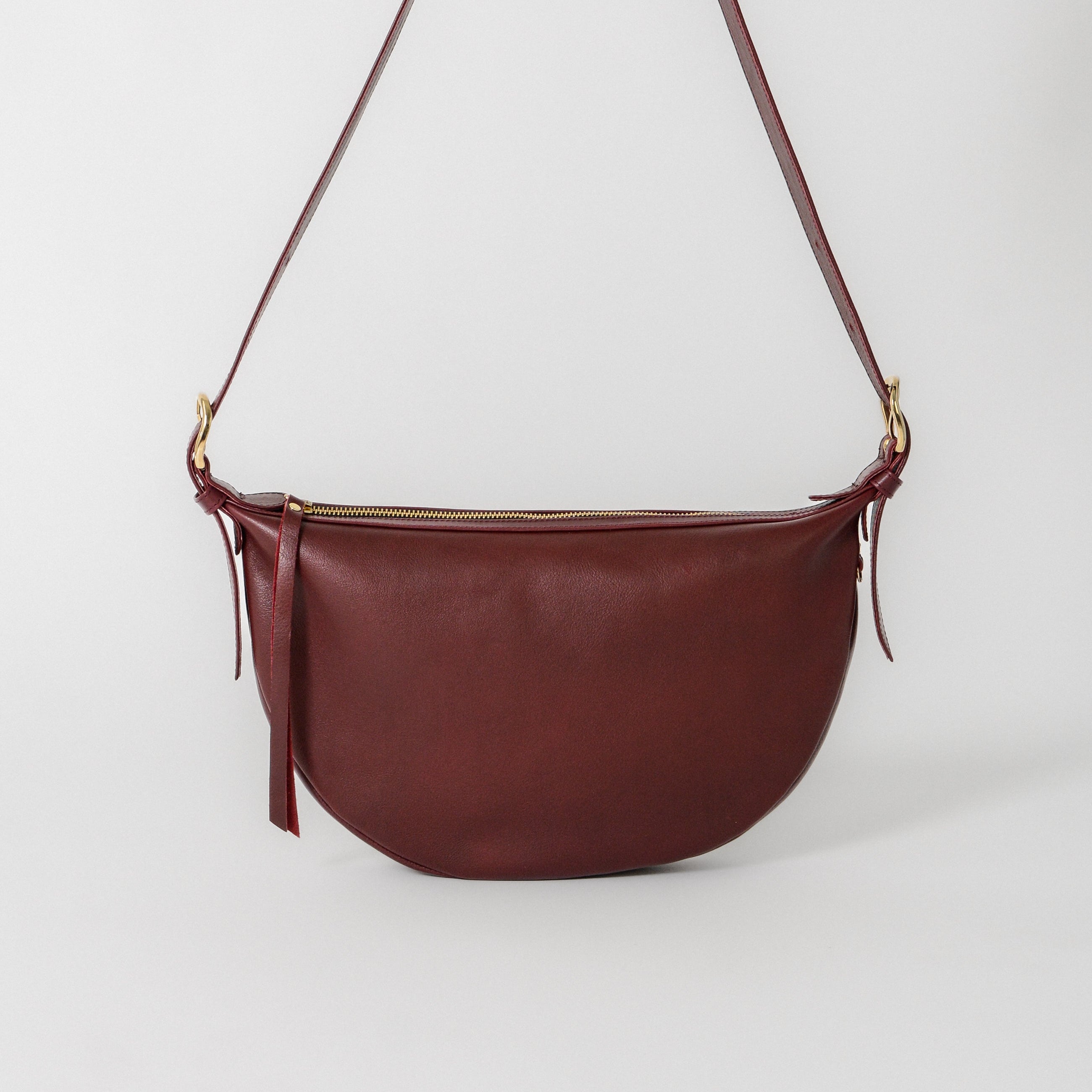 Nova Sling Bag in Pinot leather featuring a curved silhouette, adjustable strap, and zip-top closure for effortless everyday wear.