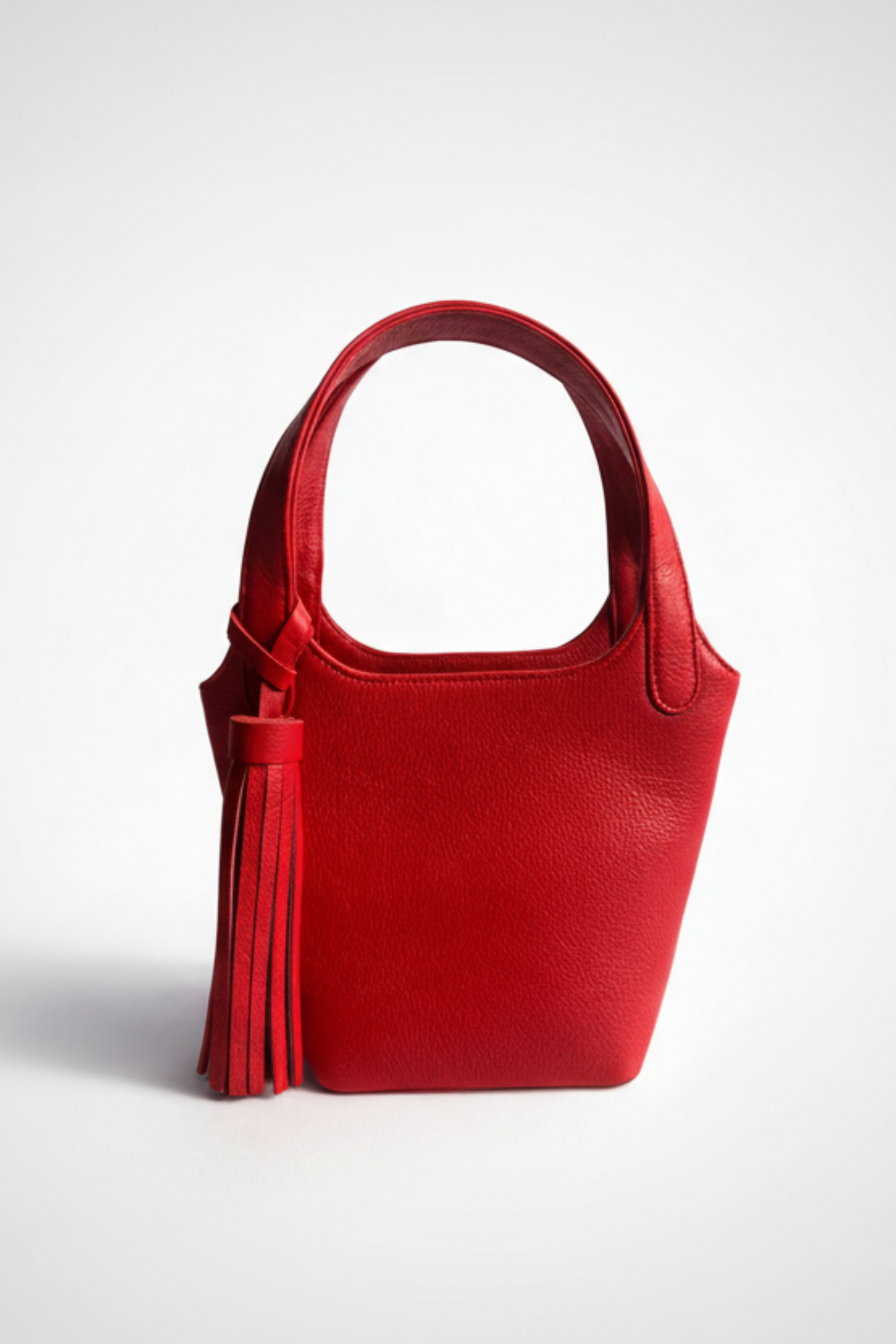 Red leather Phoebe bucket bag with top handle and tassel detail, featuring a soft structured silhouette and clean, minimalist design.